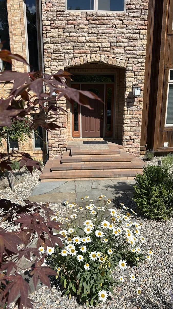 Stacked-stone archway front entry with paver steps, a Japanese maple, and white daisies in Livonia, MI