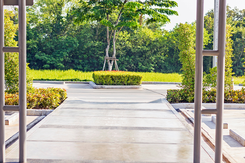 Concrete walkway through a landscaped entrance with trimmed shrubs and trees