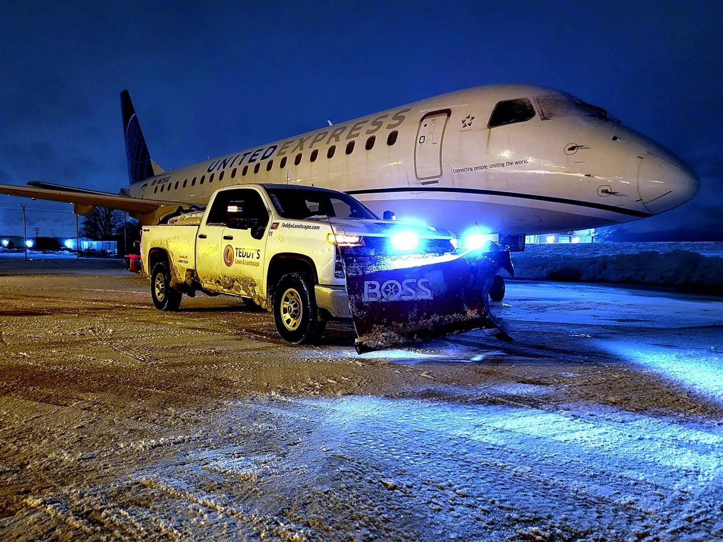 Teddy's plow truck clearing snow on an airport tarmac beside a regional jet