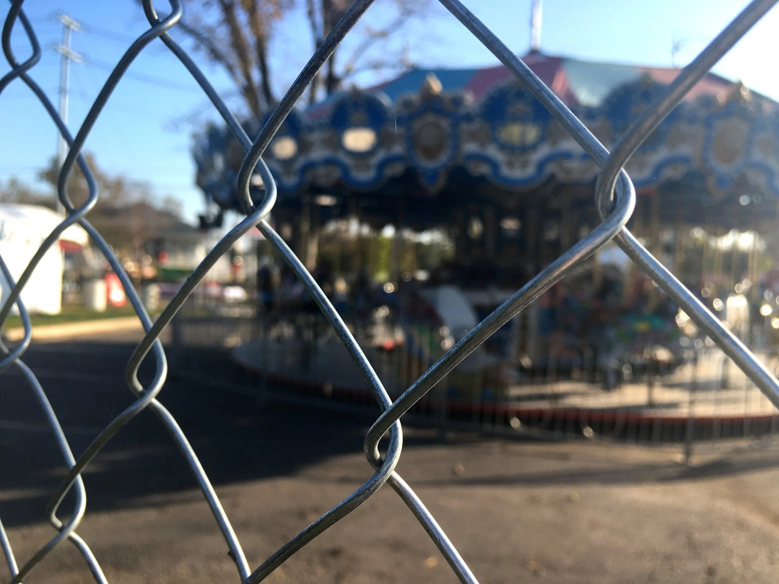Chain link fence clearly barring off a blurred marry-go-round, representing the separation felt from childhood or one's children as they age or enter menopause
