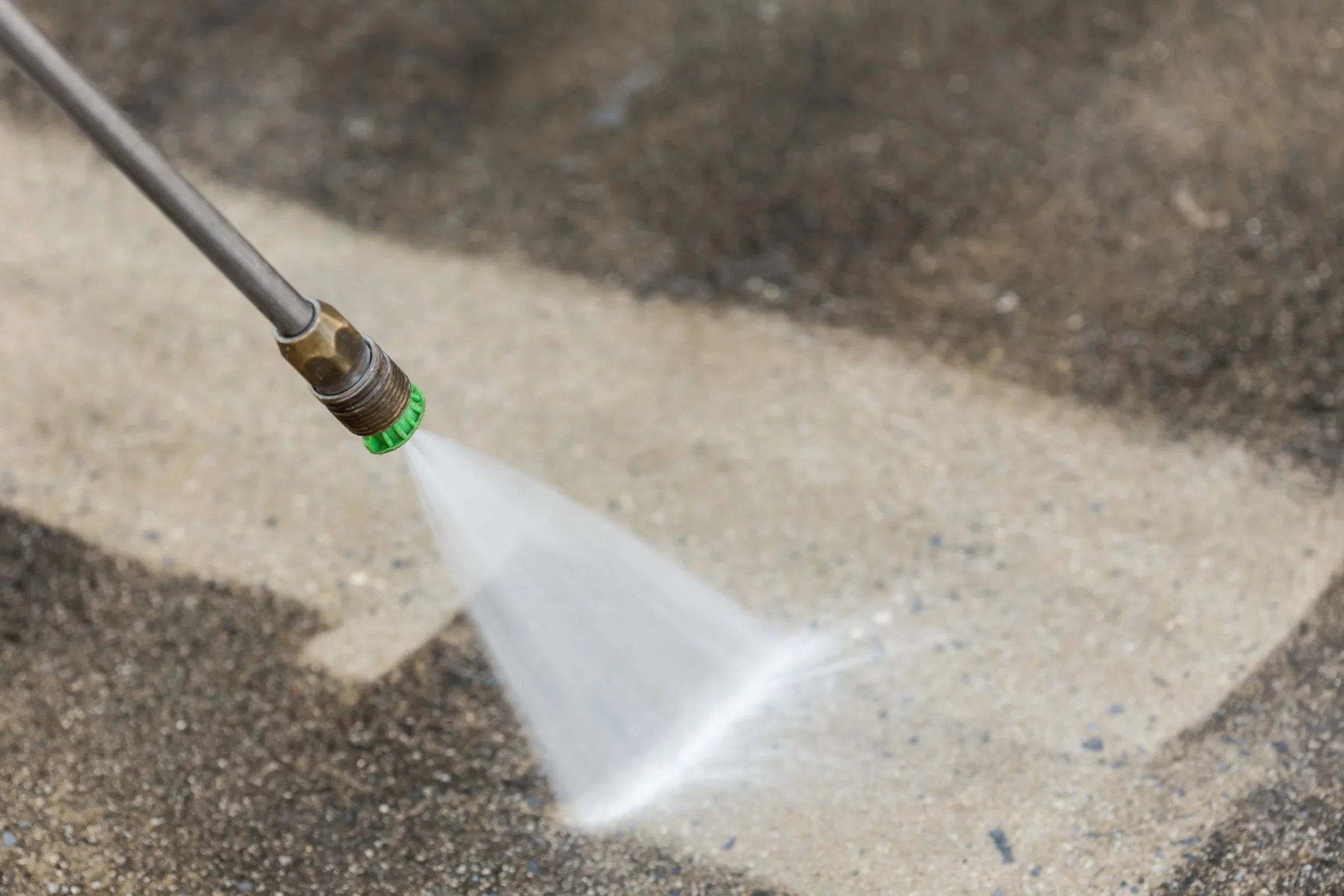 A pressure washer nozzle spraying water onto a concrete surface.