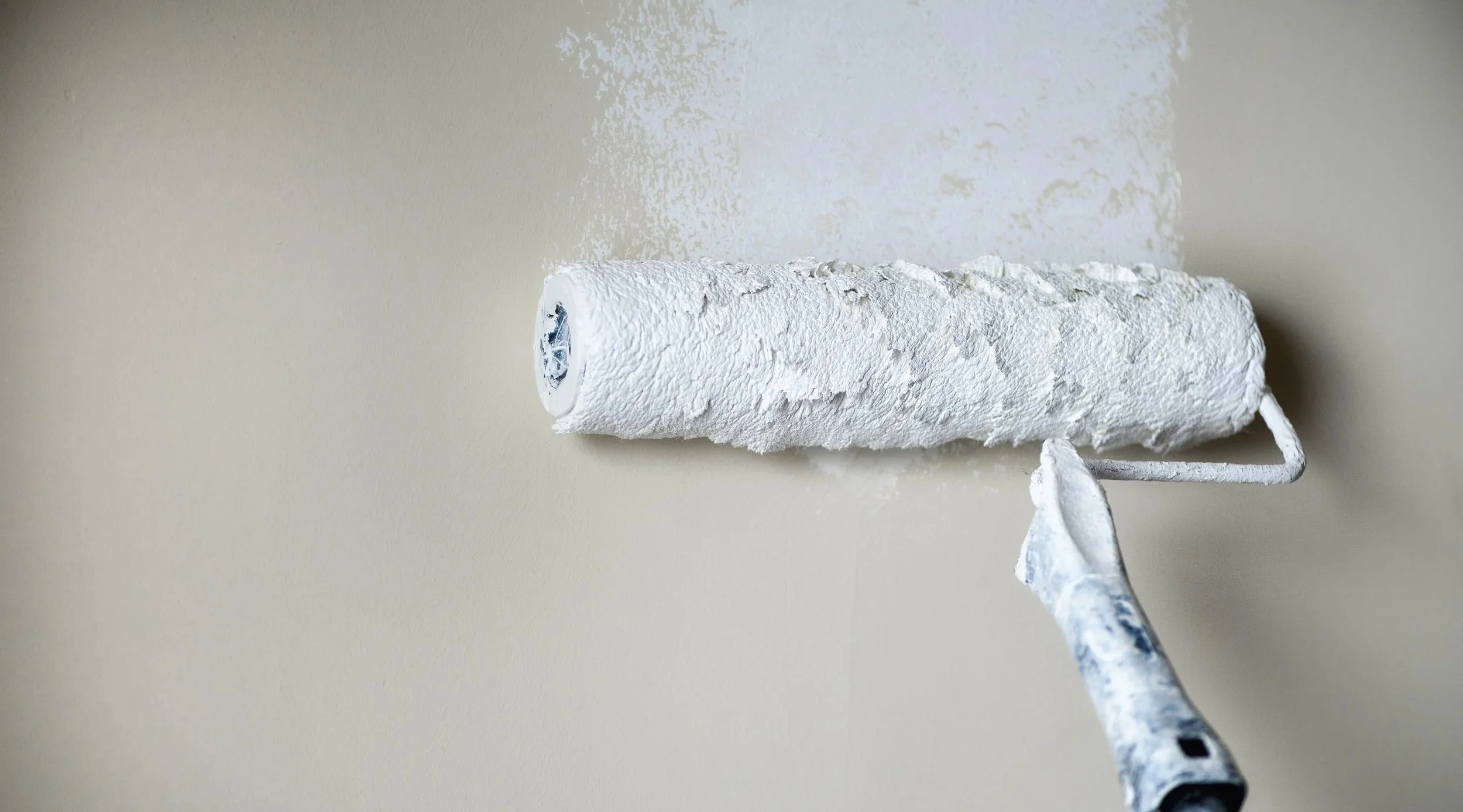 A paint roller applying white paint on a wall.
