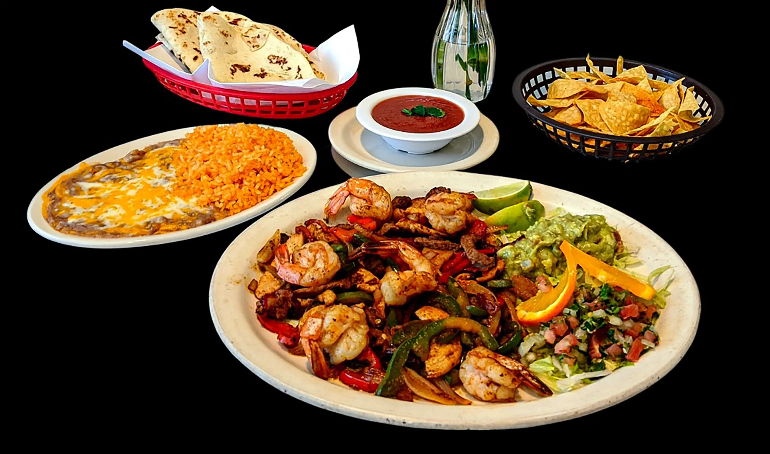 A variety of Mexican dishes on plates and baskets, including shrimp fajitas with peppers and onions, Mexican rice, refried beans topped with