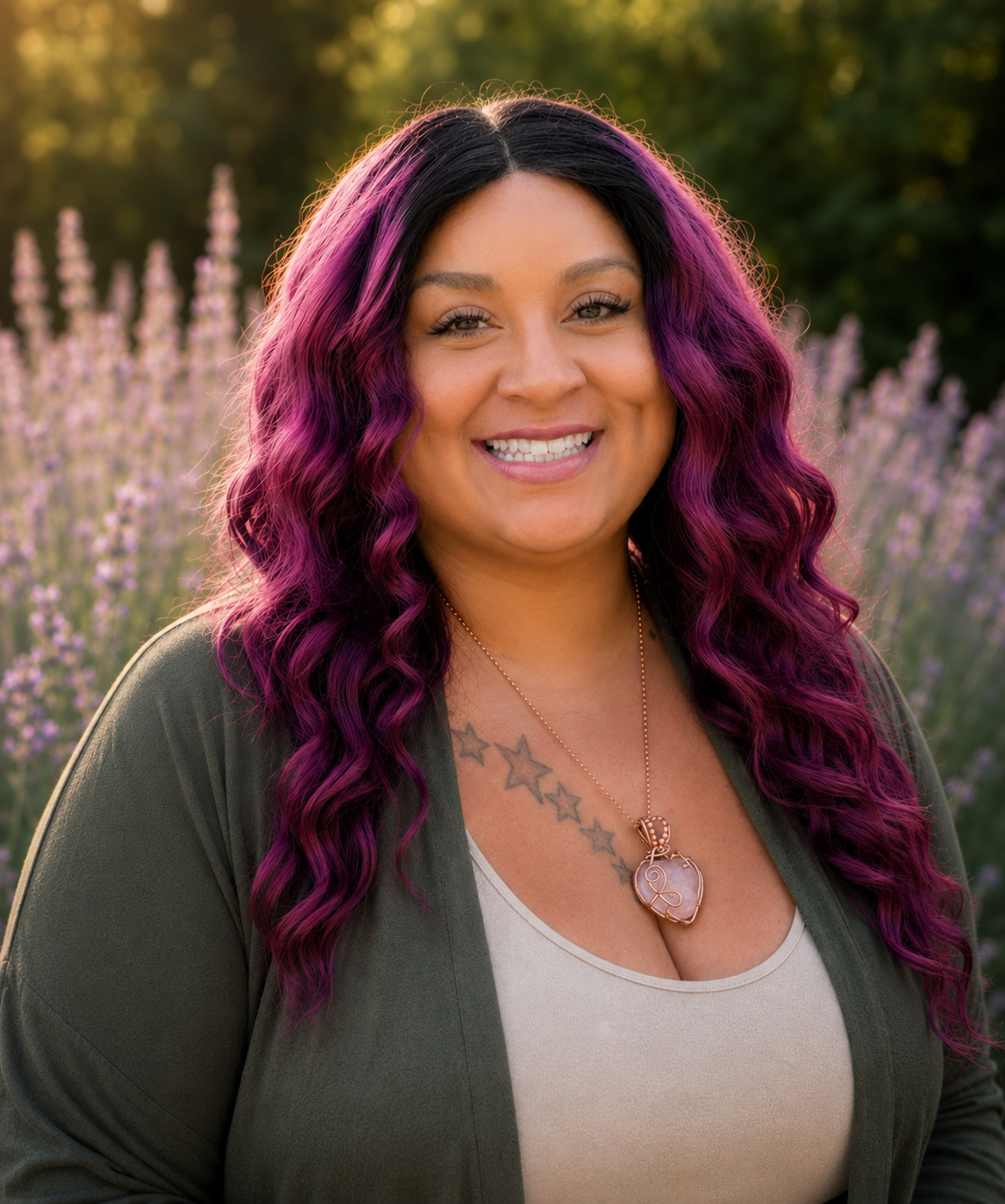 A woman with long, wavy purple hair outdoors, smiling at the camera, wearing a white top and a necklace with a heart-shaped pendant, surrounded by purple flowers and green trees in the background.