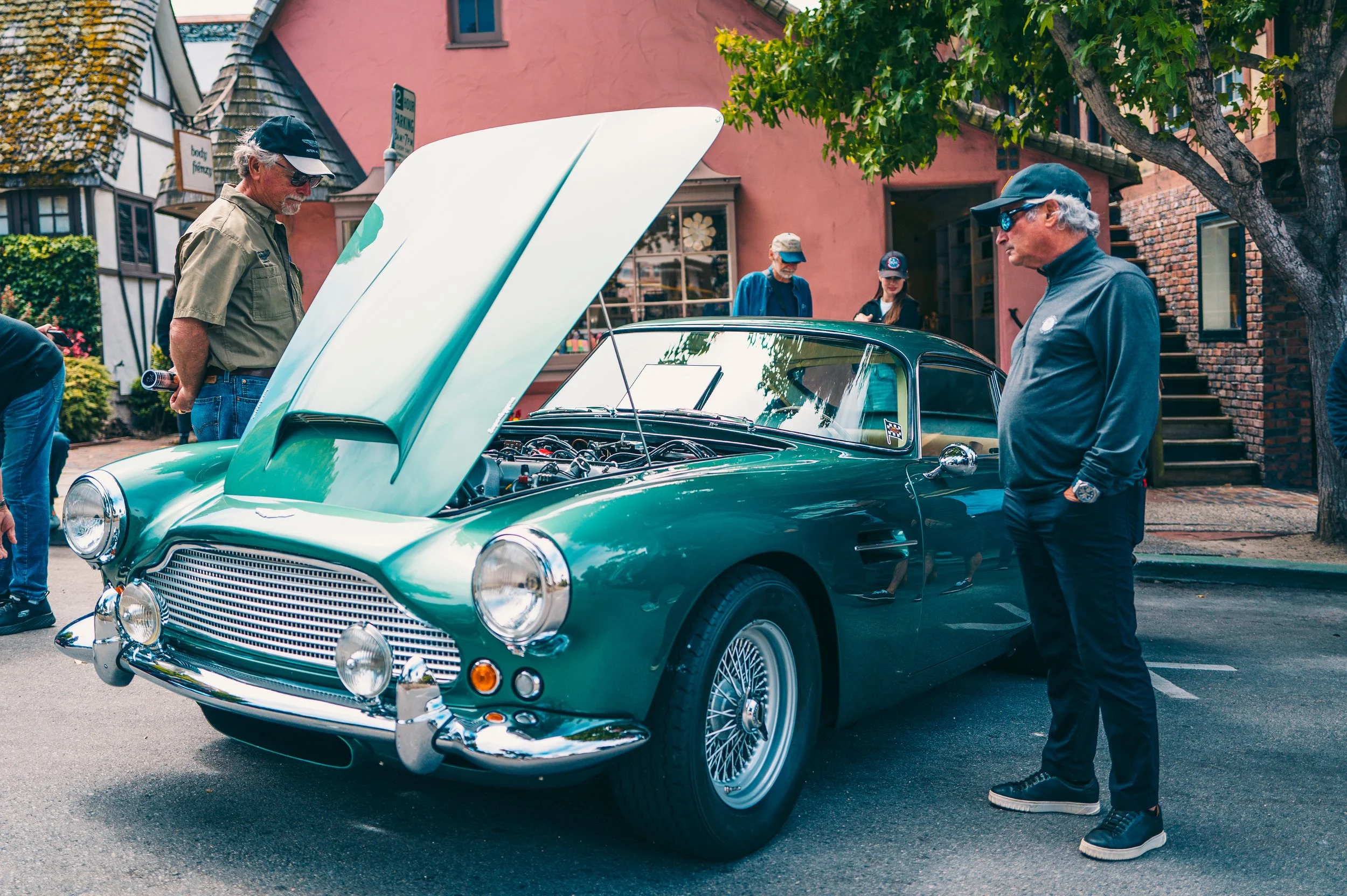 A group of people admiring a vintage green car with its hood open on a city street during a car show.