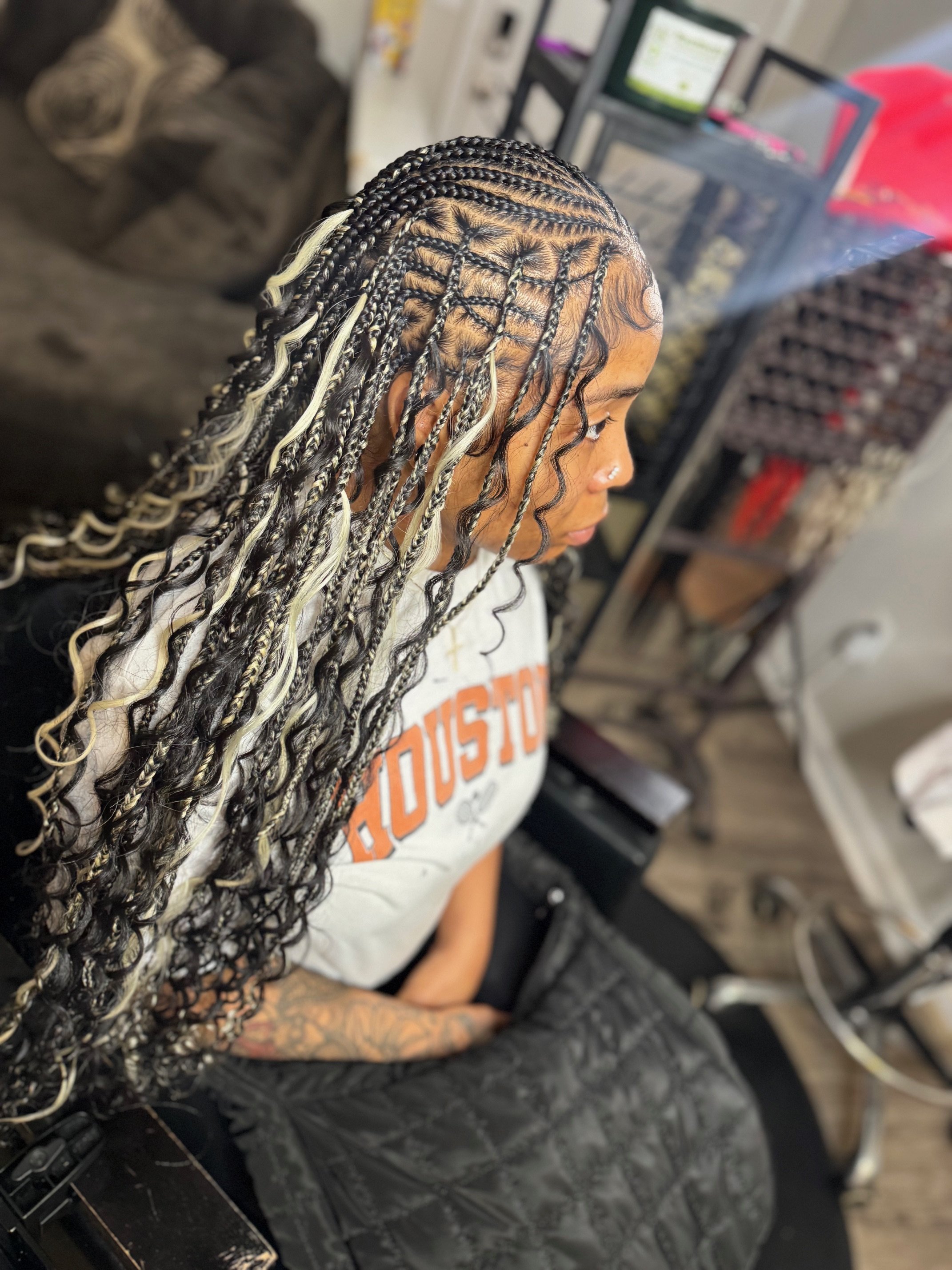 A woman with long, black and blonde foam box braided hair, sitting in a salon chair.