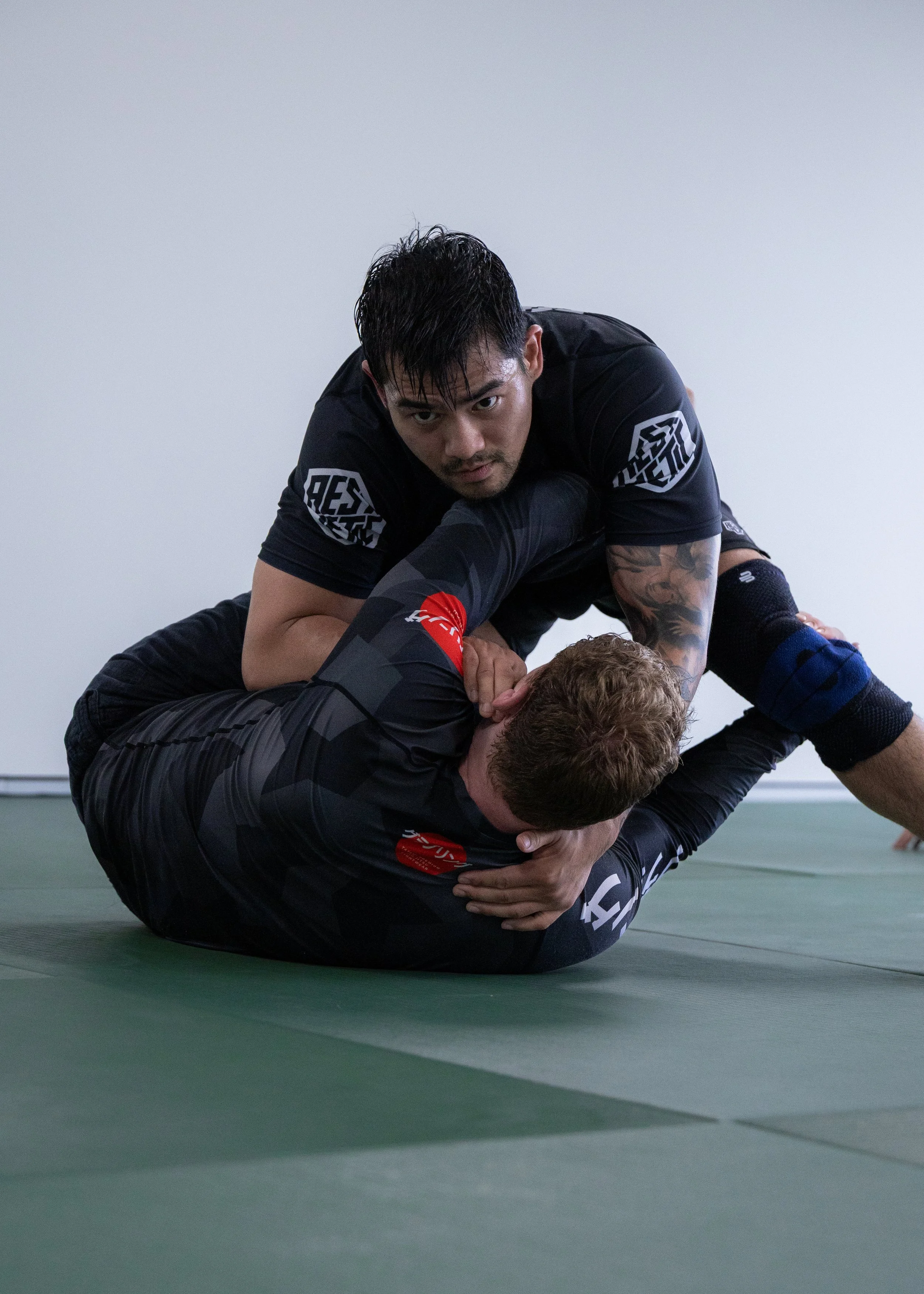 Two men practicing Brazilian Jiu-Jitsu on a green mat, with one man applying a chokehold on the other.