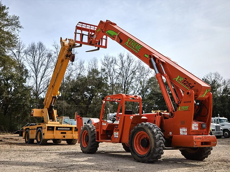 A large orange telescopic boom lift with the label 'XR 1254' is extended in an outdoor lot with other construction vehicles and bare trees in the background.