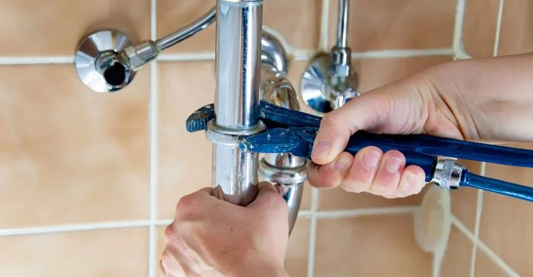 Person repairing a plumbing pipe with a wrench and tubing in a tiled bathroom.