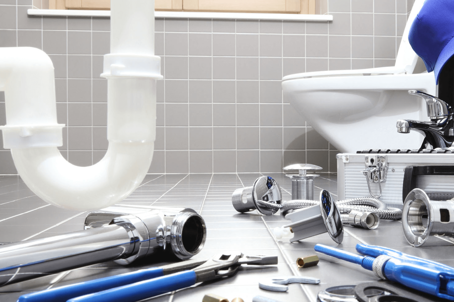 Disassembled plumbing pipes, tools, and parts on a tiled bathroom floor near a toilet.