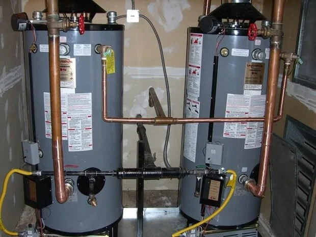 Two water heaters with copper and yellow flexible pipes in a utility room.