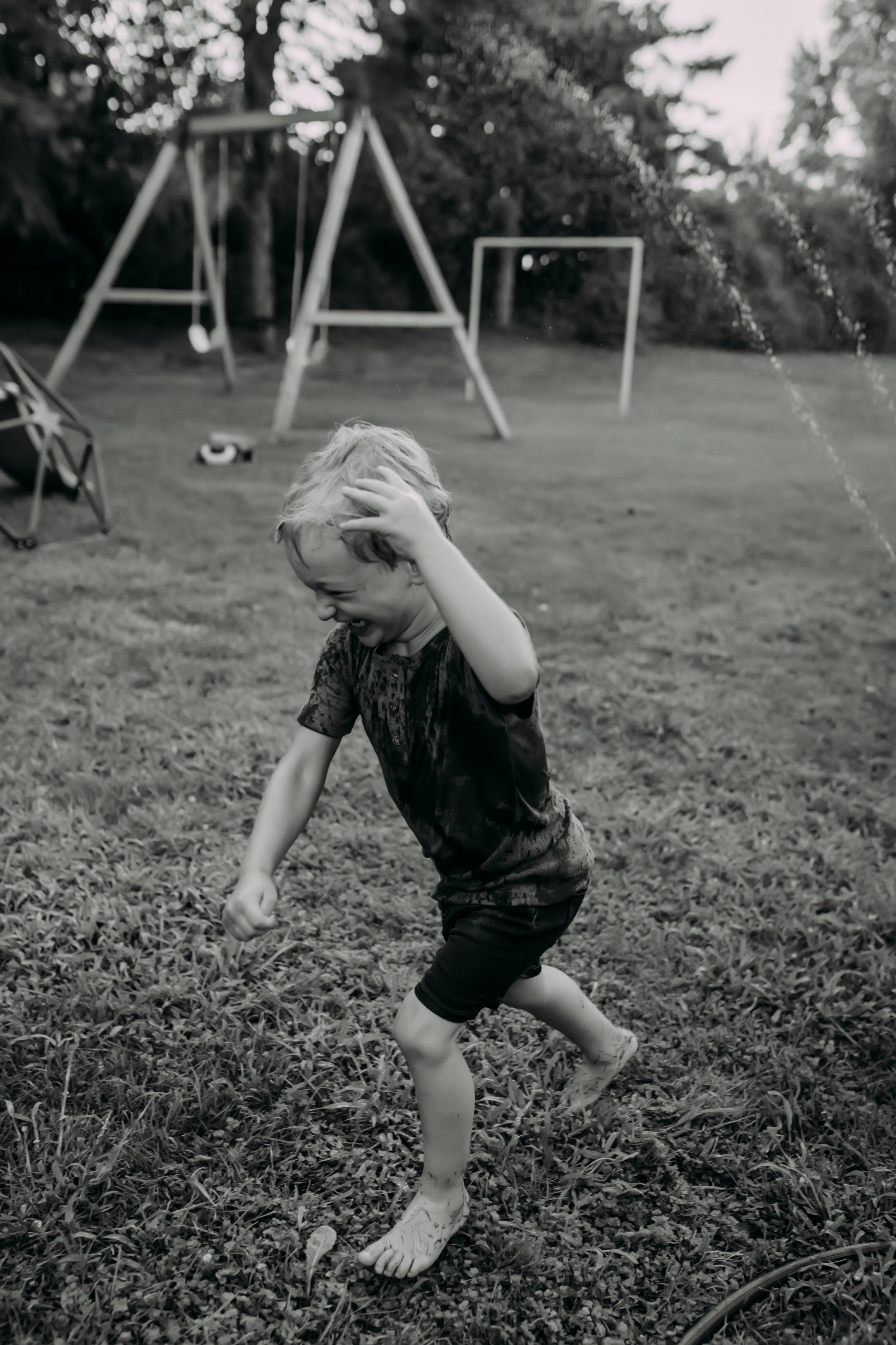 Child running through the sprinkler laughing during family photography session documentary style