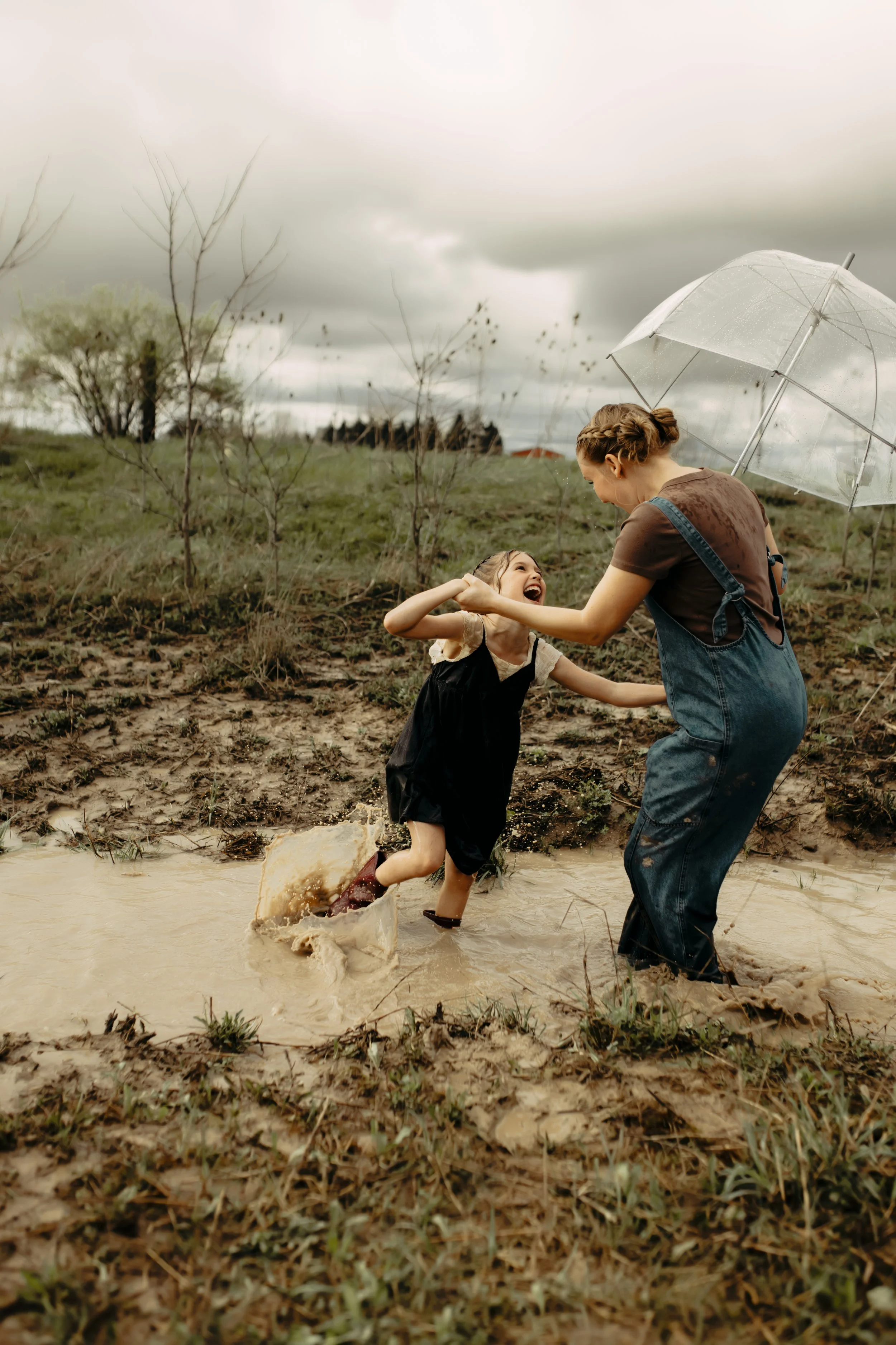 Family photography session in Hudsonville, Michigan with Mom and daughter laughing while splashing in puddles during storytelling session