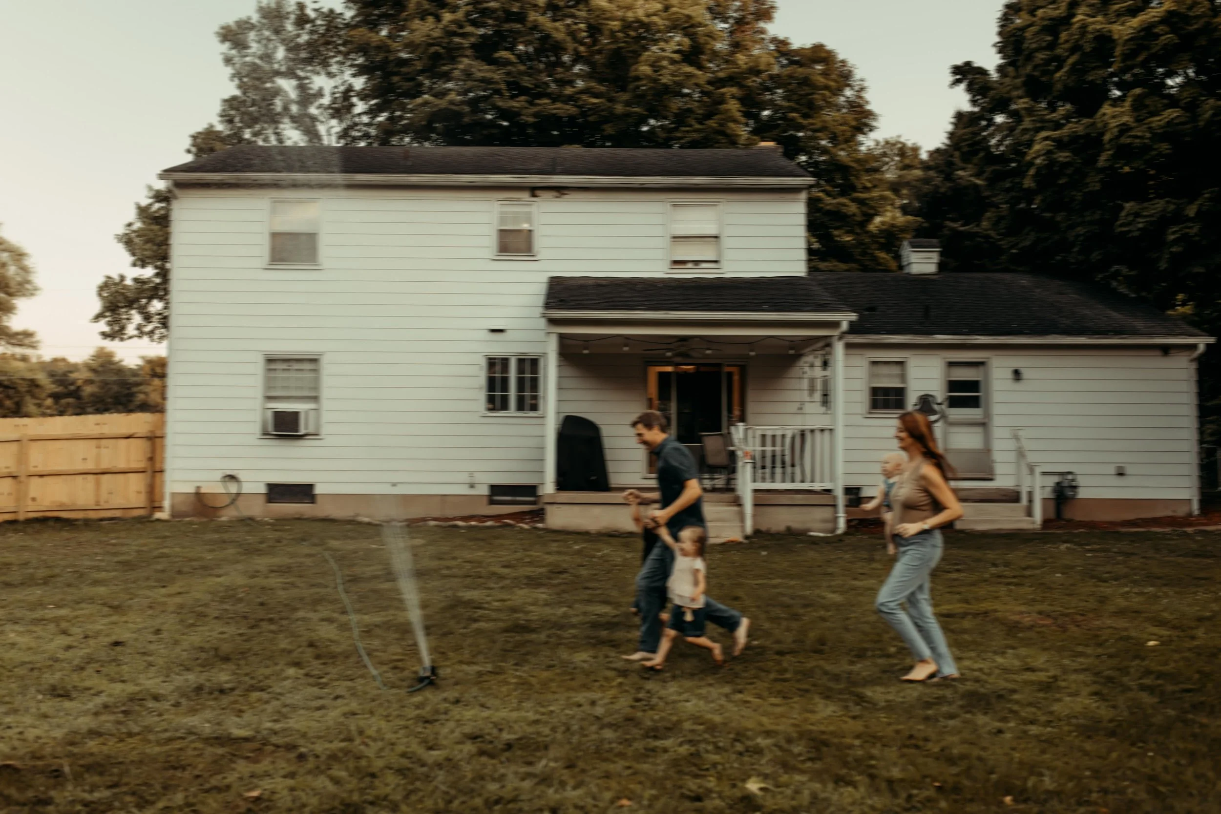 family playing in their backyard running through sprinklers during documentary photography session