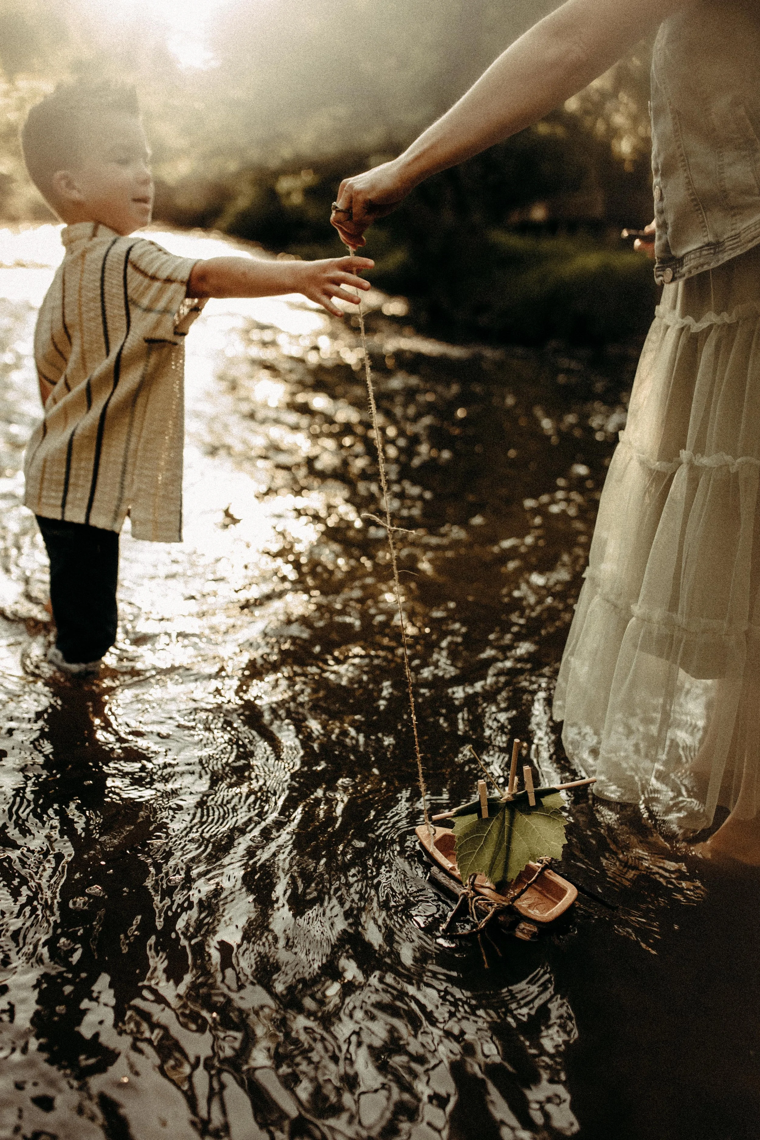 mother and son experiencing a favorite childhood activity playing with boats at the creek during grand rapids documentary photography session