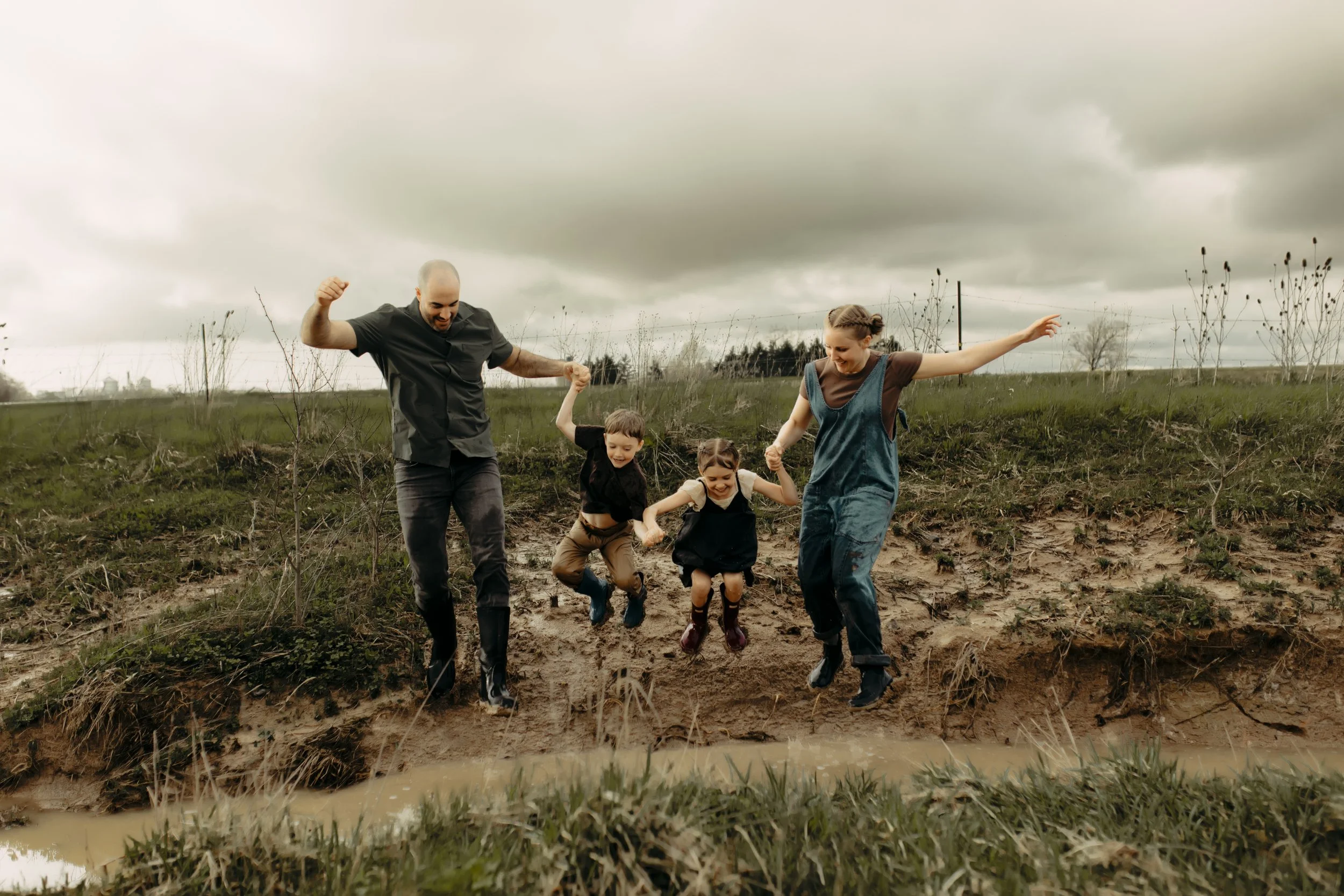 Family photography session in Hudsonville Michigan with a family jumping in puddles during storytelling family photography session