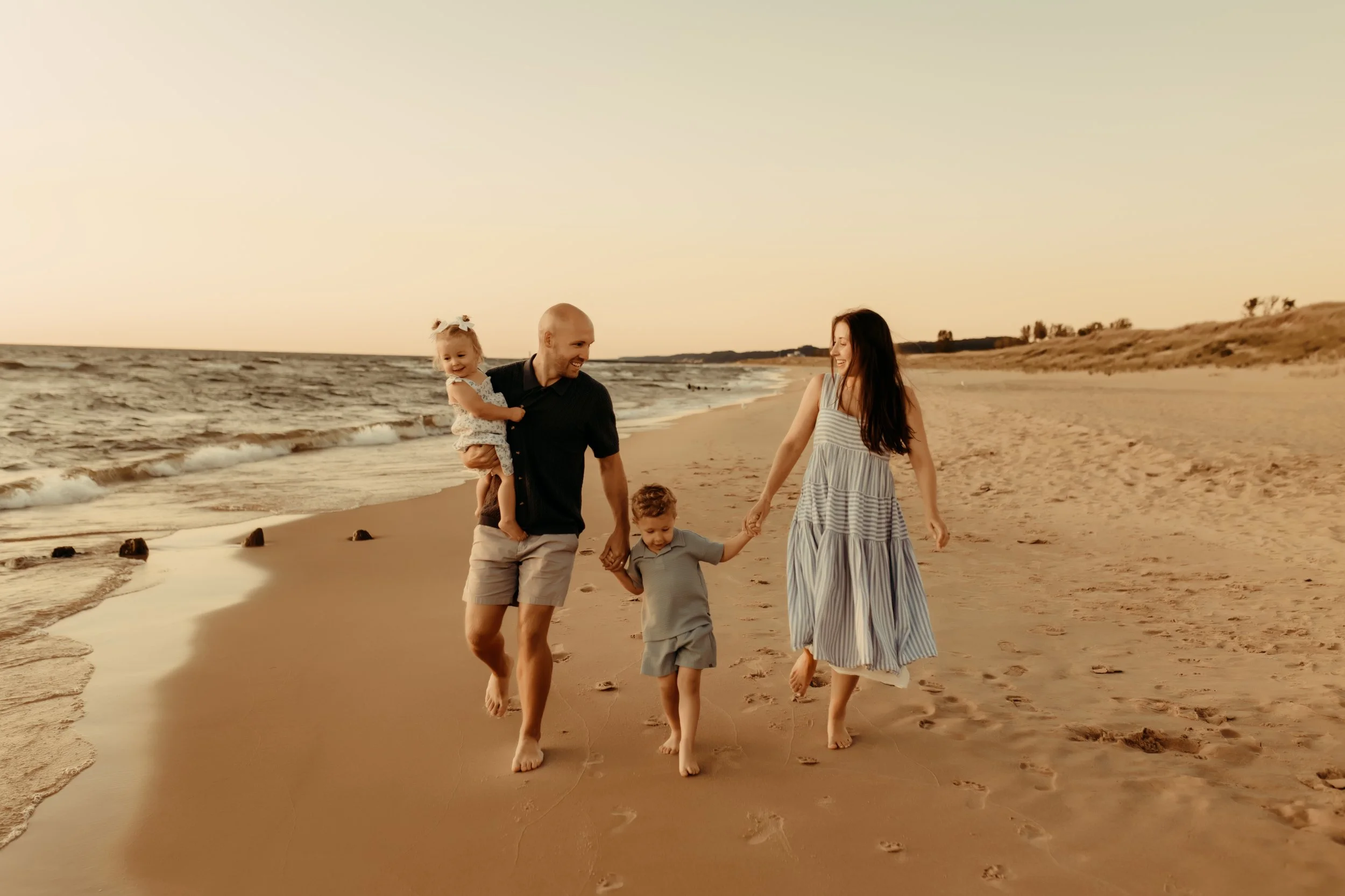Family walking along the beach hand in hand smiling along lake Michigan in Holland, Michigan