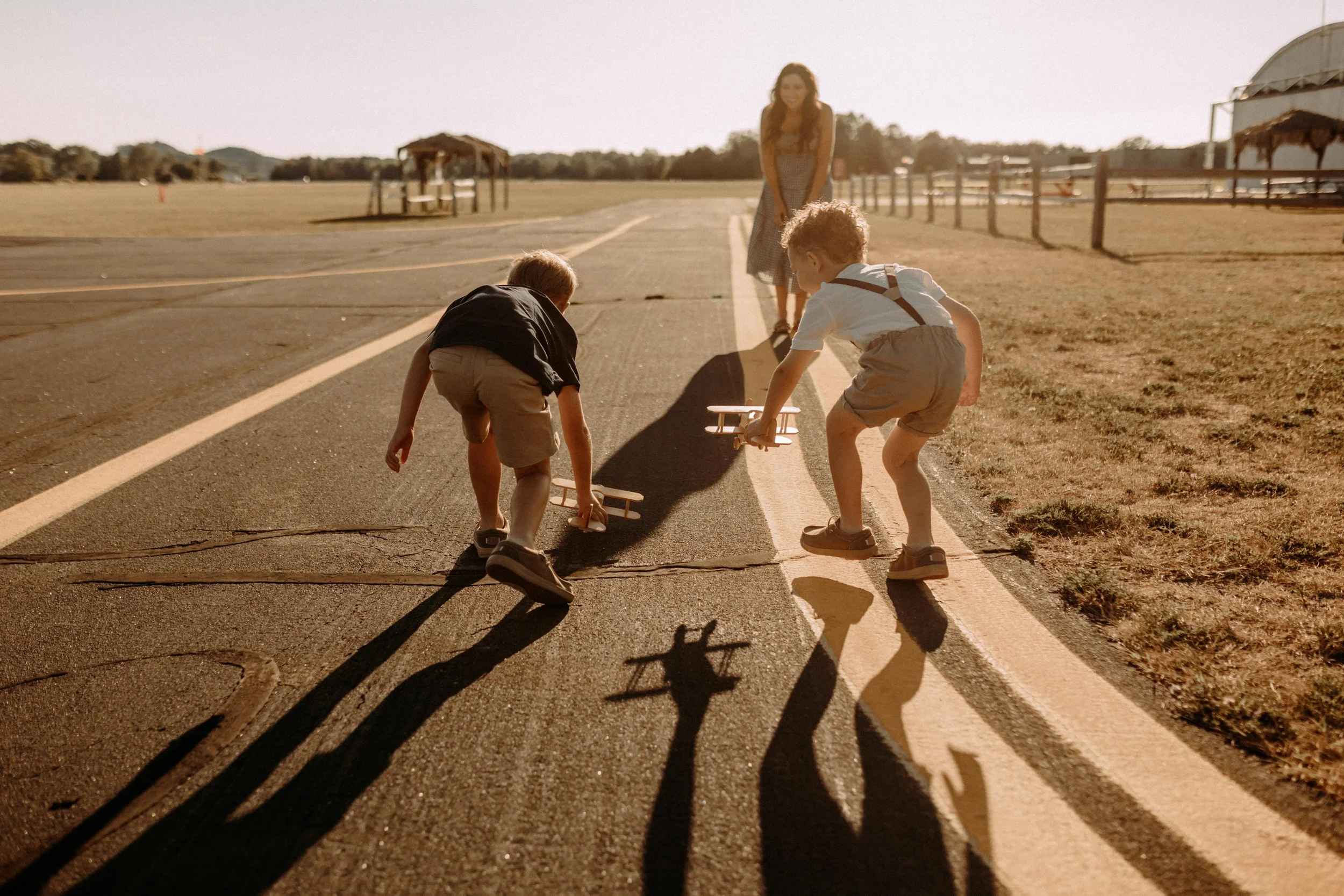 boys playing with wooden airplanes at the airport with their mom during family photography session