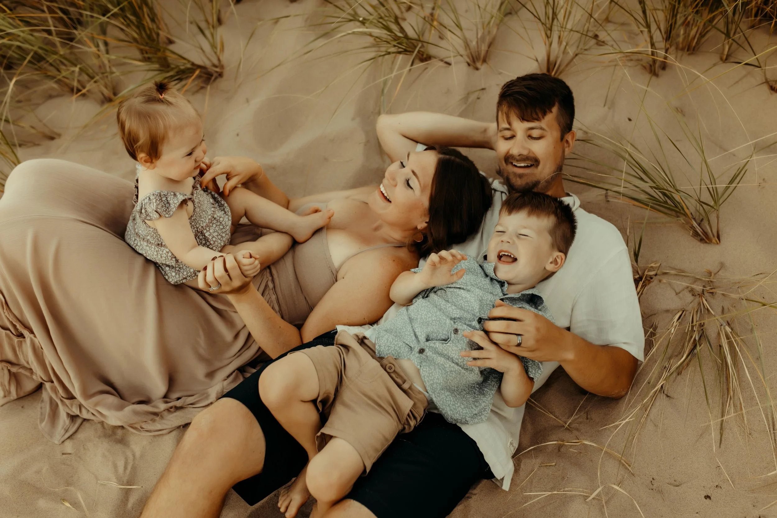 Family laughing on the Oval Beach sand dunes during a documentary family photography session in the summer in Michigan