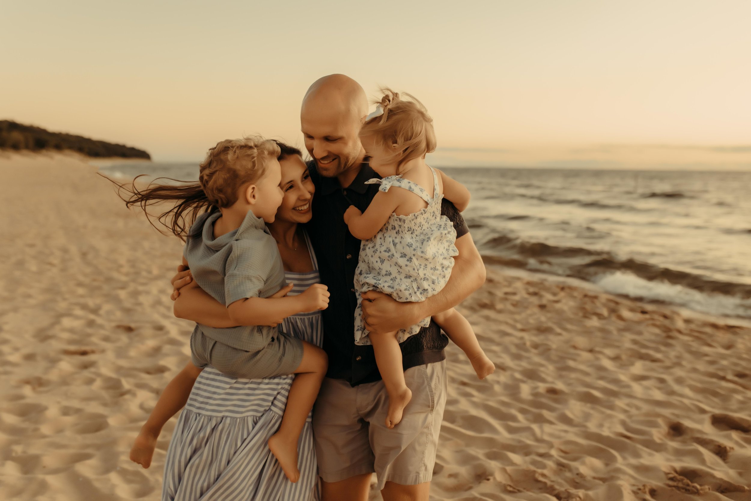 Family smiling at each other along the lakeshore at Oval beach in Saugatuck, Michigan during a summer photography session