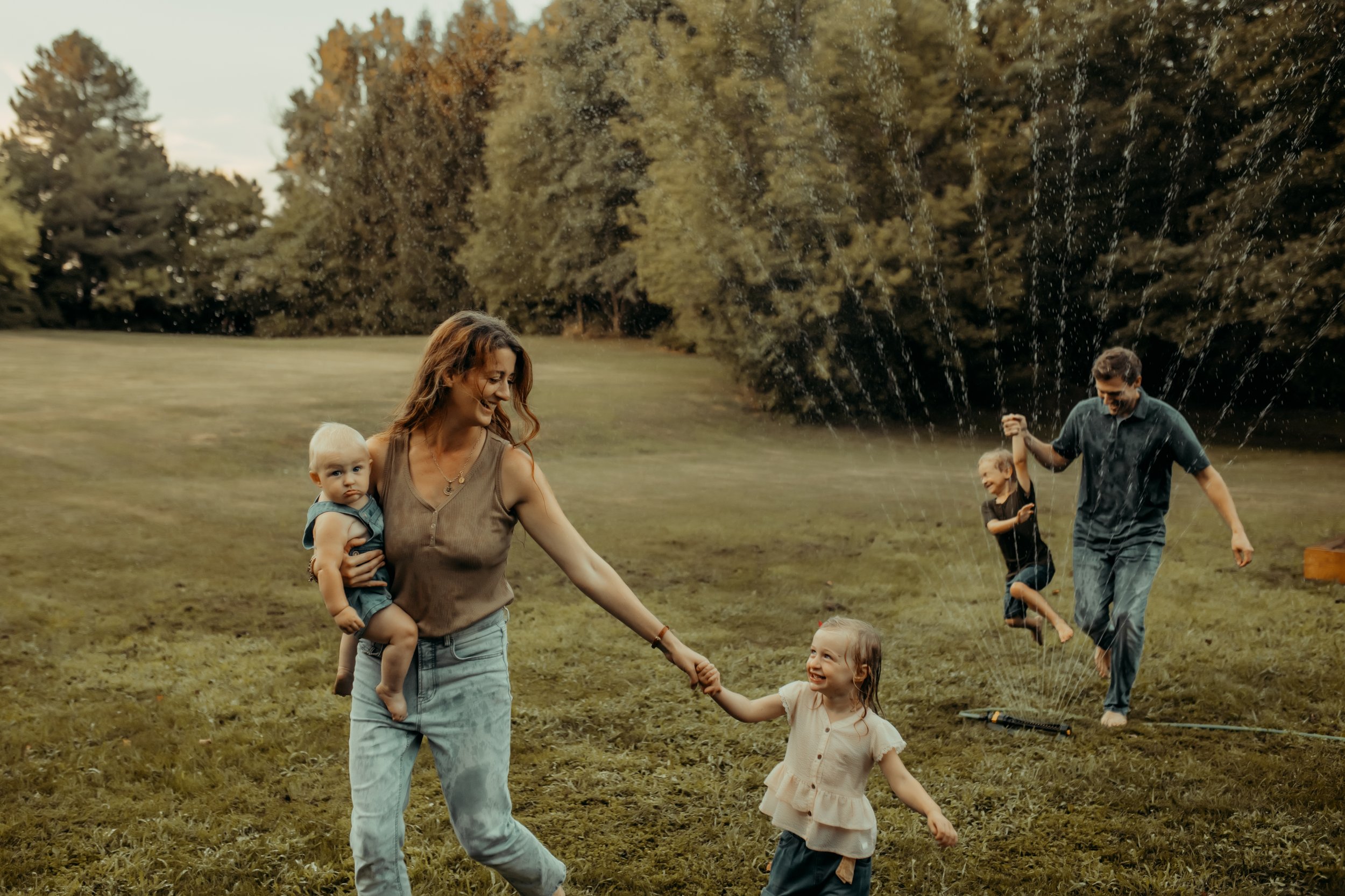 Family running through the sprinkler and laughing during documentary photography session