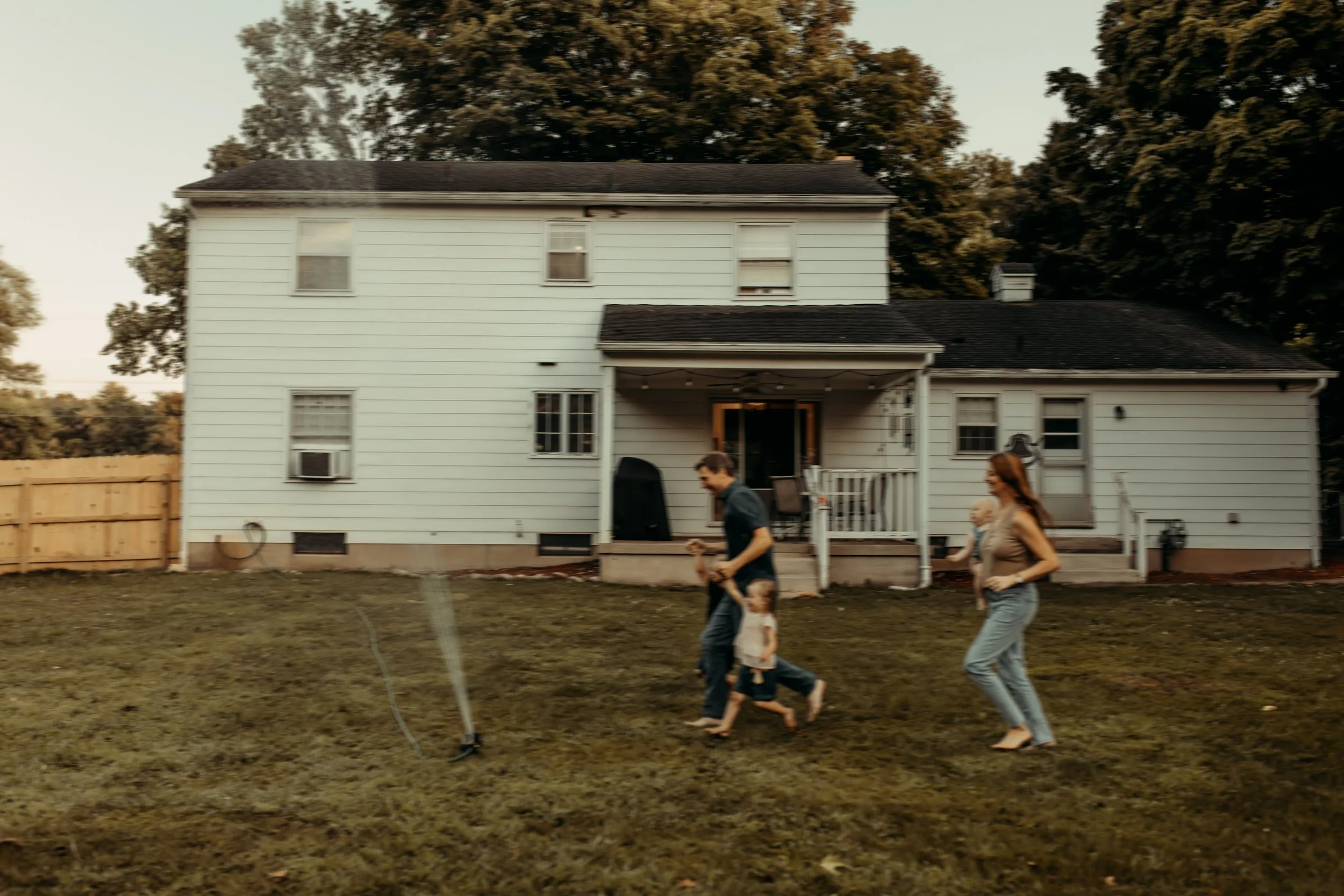 Family playing in the backyard sprinklers in the summer