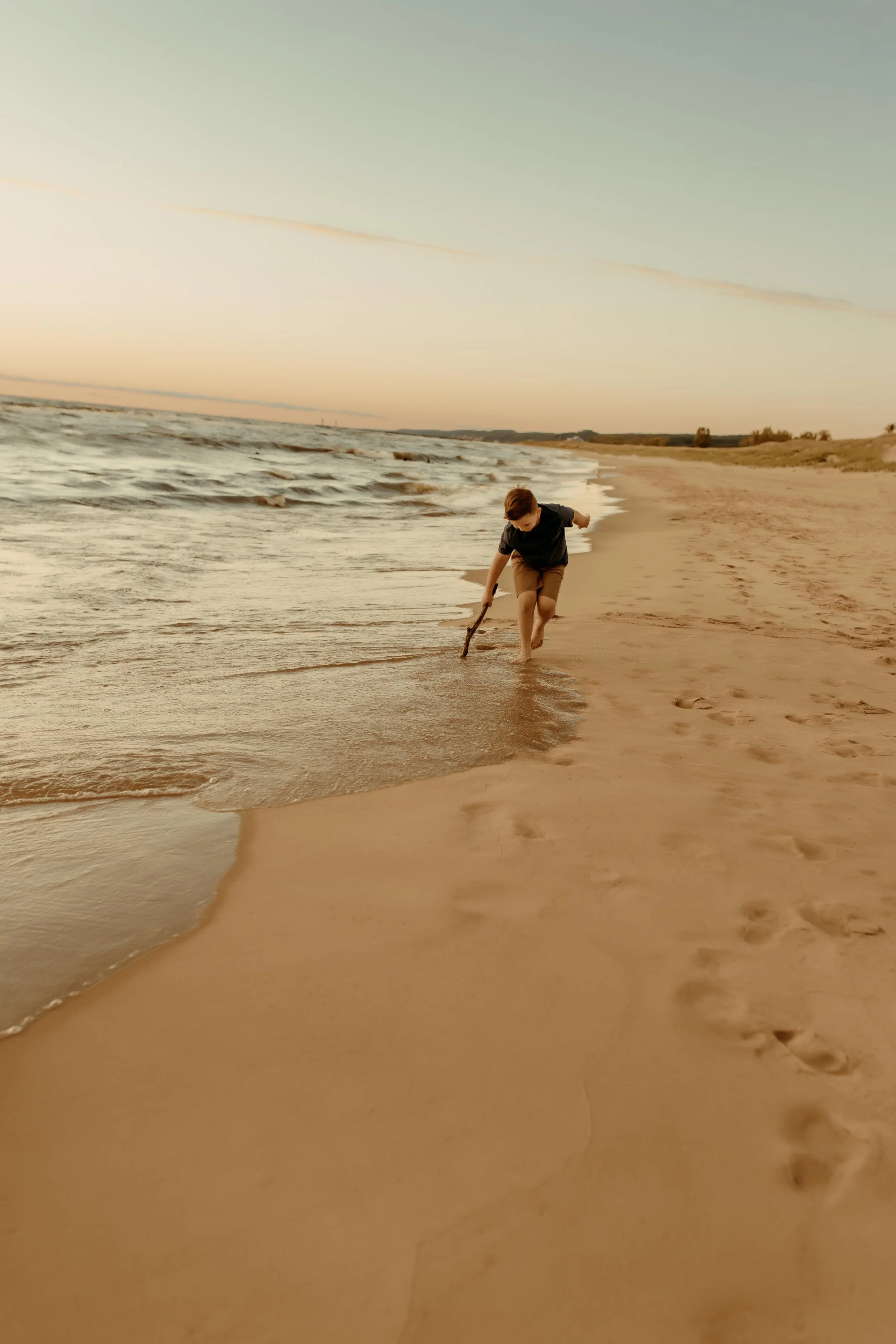 Child playing with stick along the shoreline at Oval Beach in Saugatuck, Michigan during a summer photography session