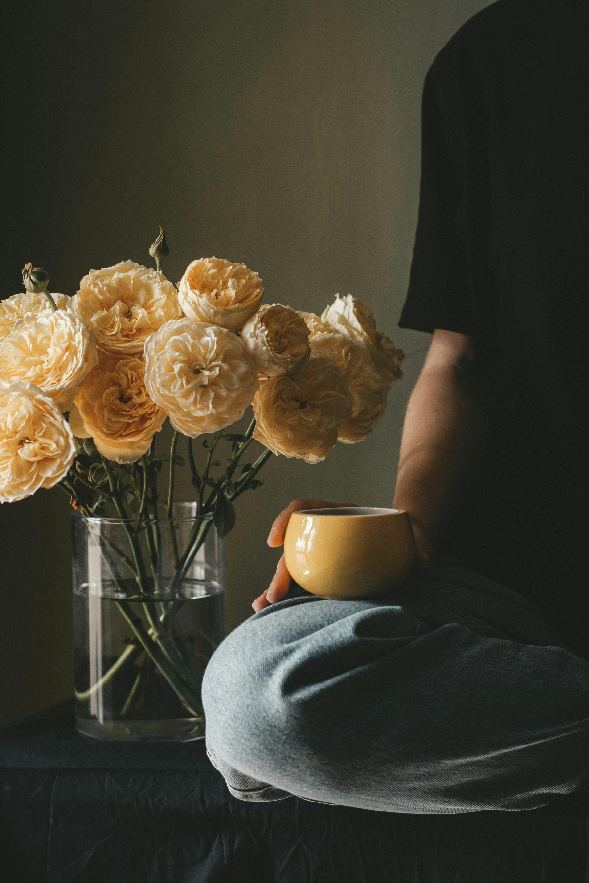 Person holding a yellow mug sitting near a vase of cream-colored roses.