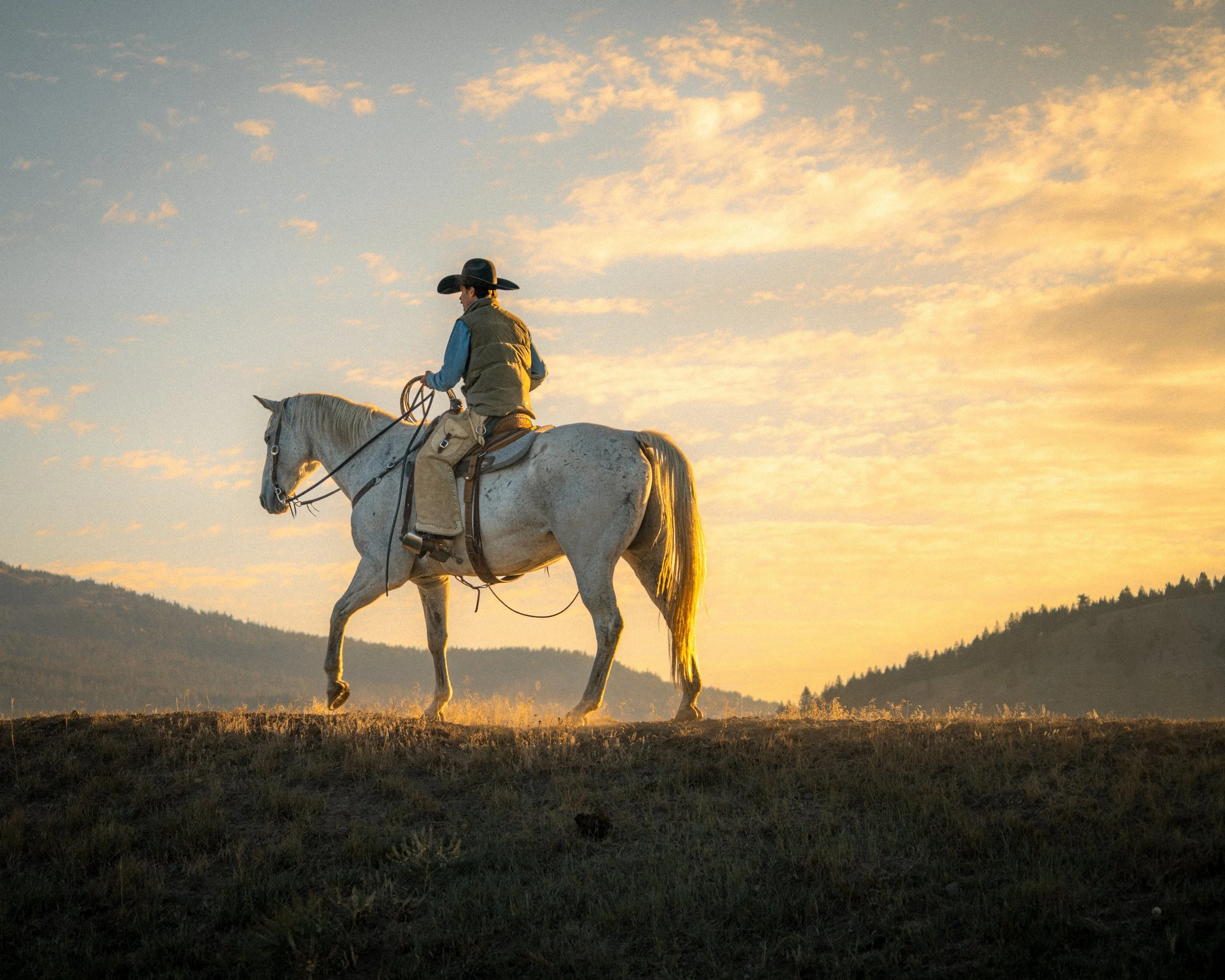 photo of cowboy riding his horse across a ridge line with a golden sunrise