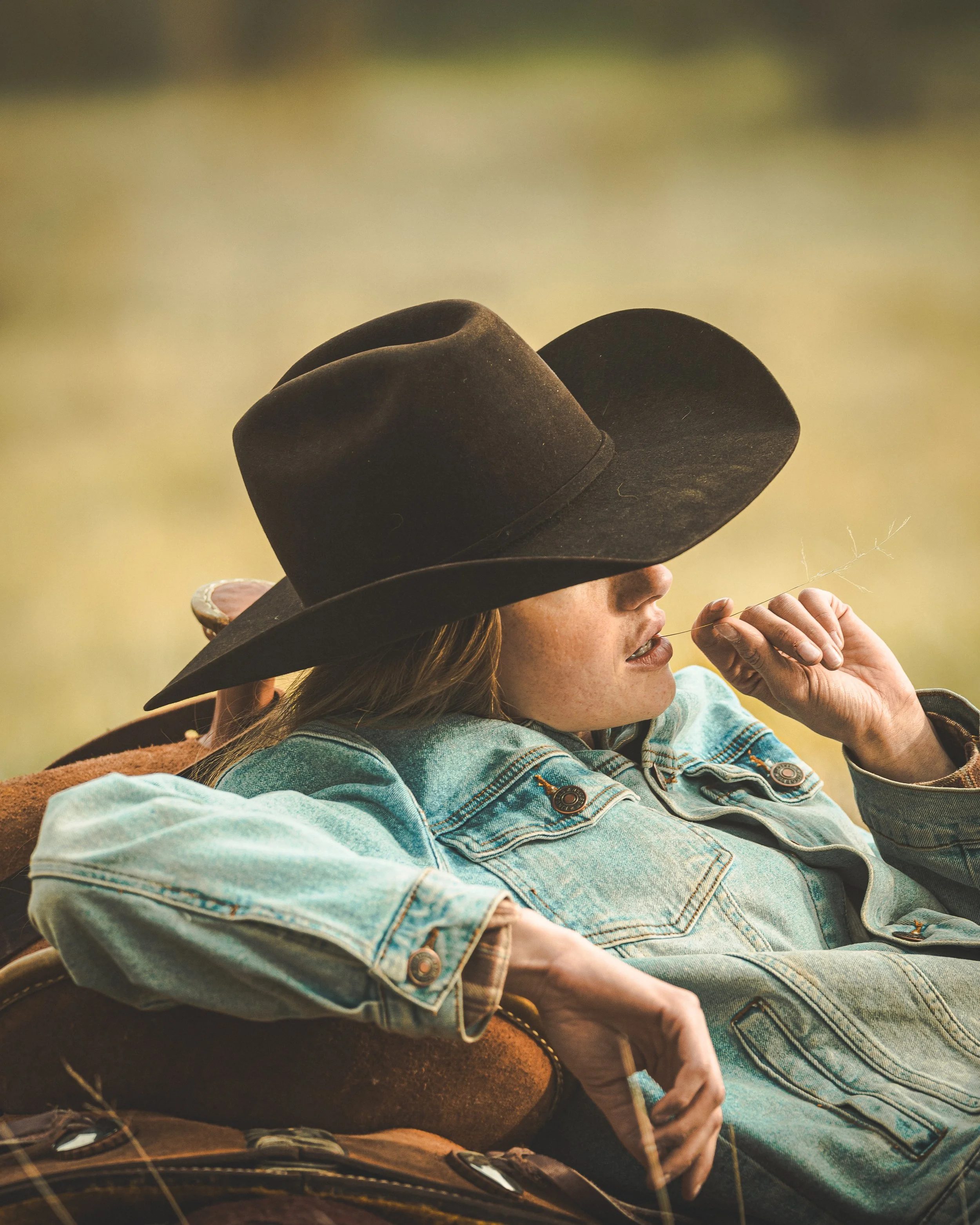 cowgirl laid back in field with grass in mouth
