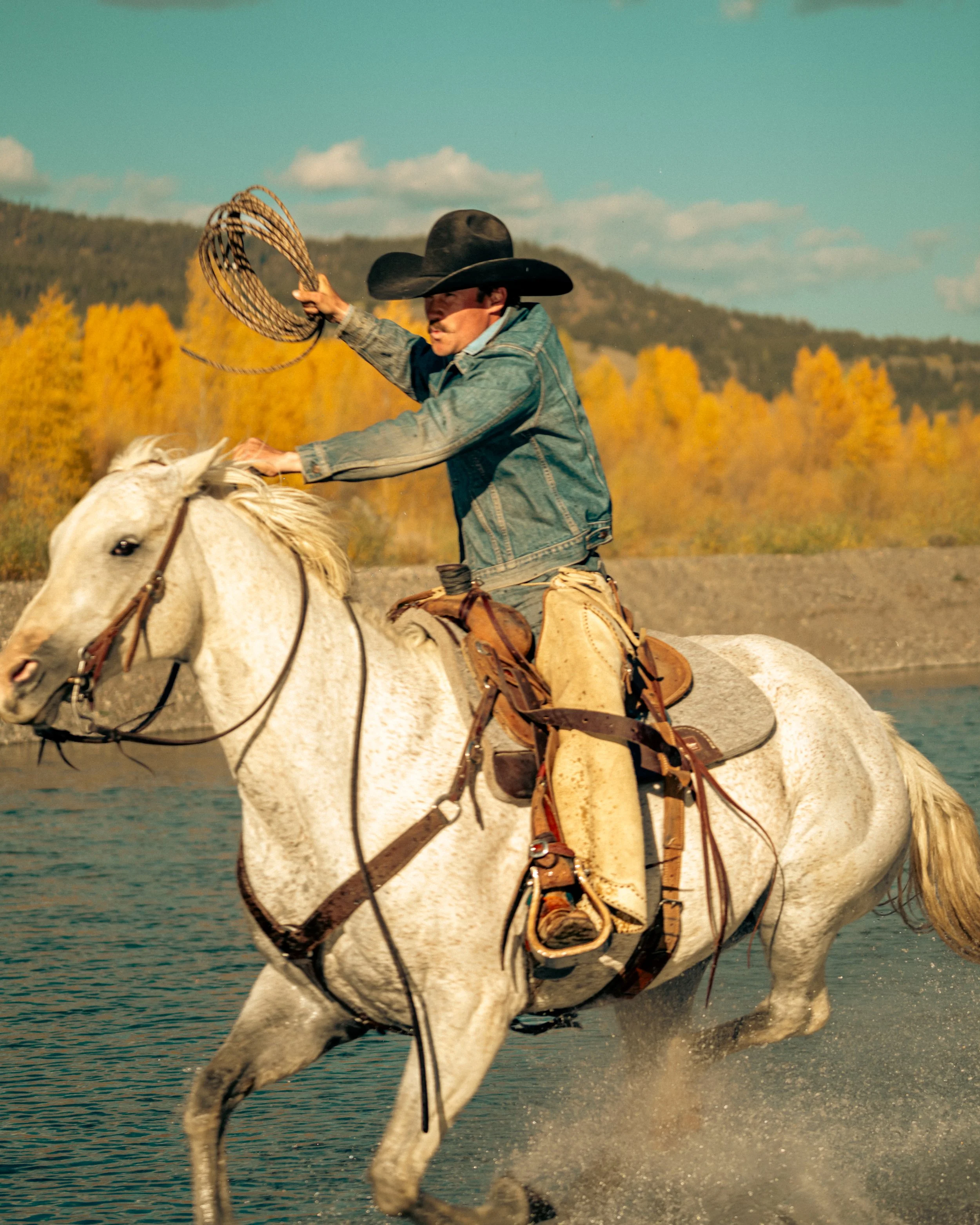 photo of cowboy riding horse through river