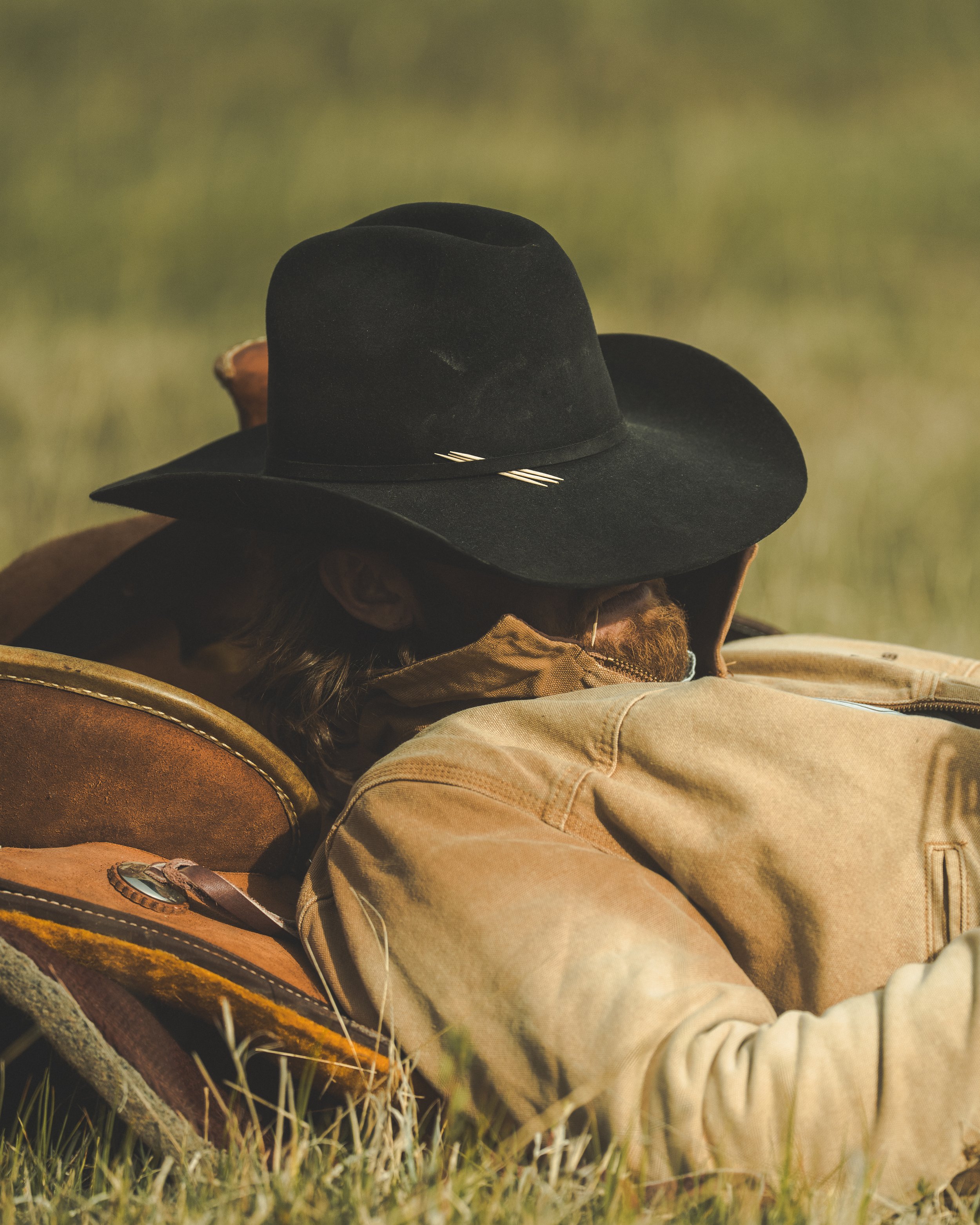 cowboy with hat over eyes laying in field taking nap