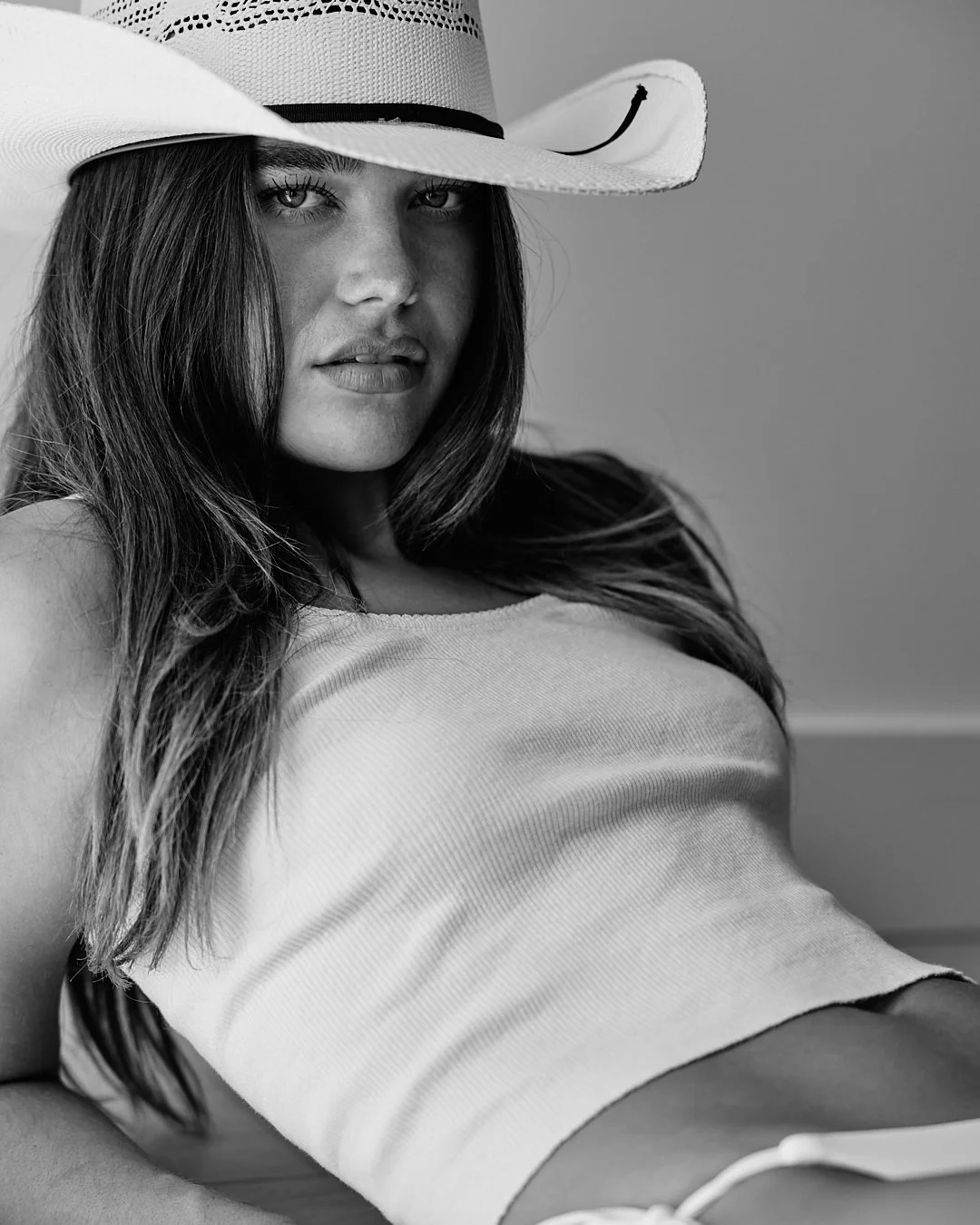A woman with long hair wearing a large cowboy hat and a sleeveless top, looking at the camera in black and white.