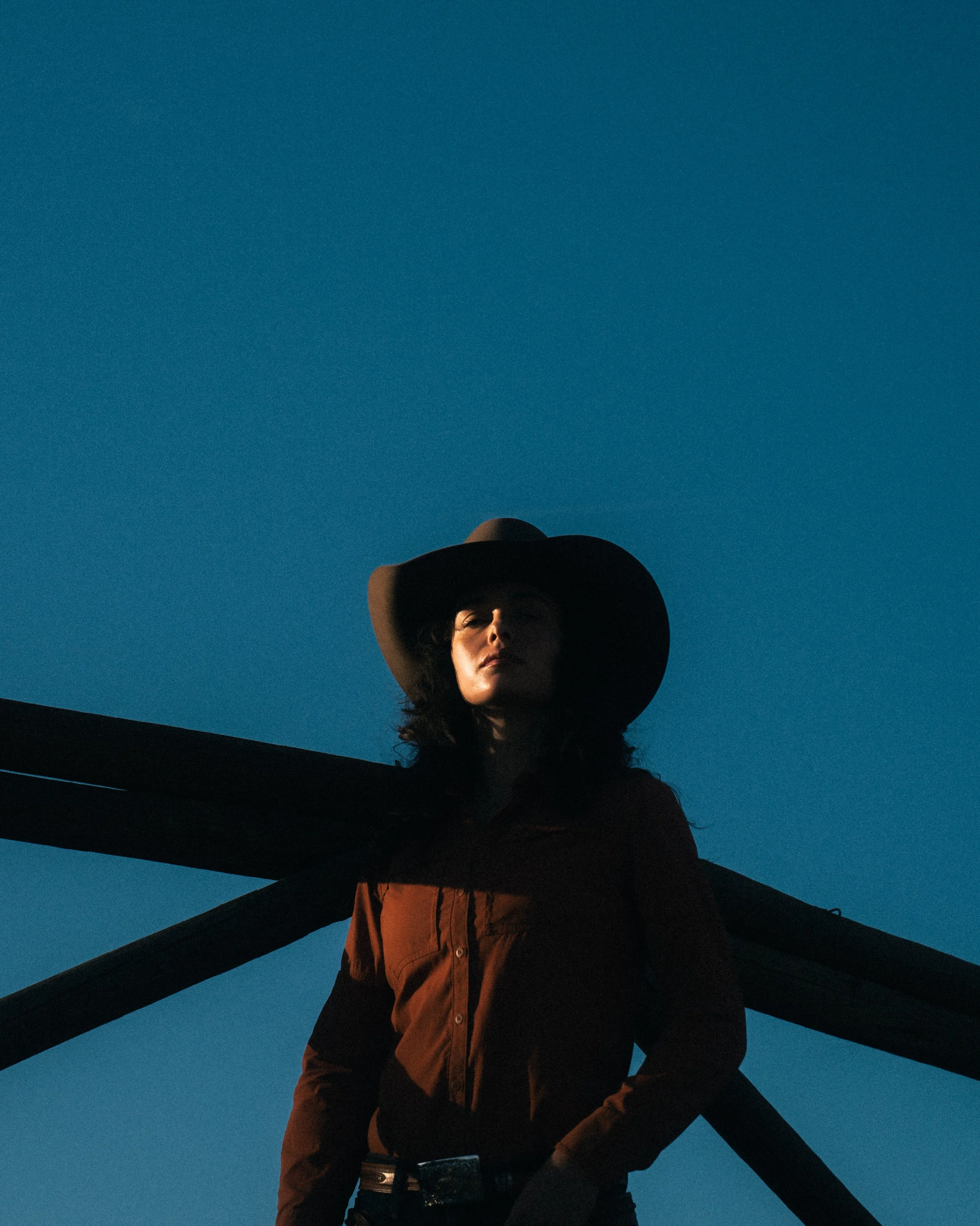 cowgirl standing in front of ranch fence