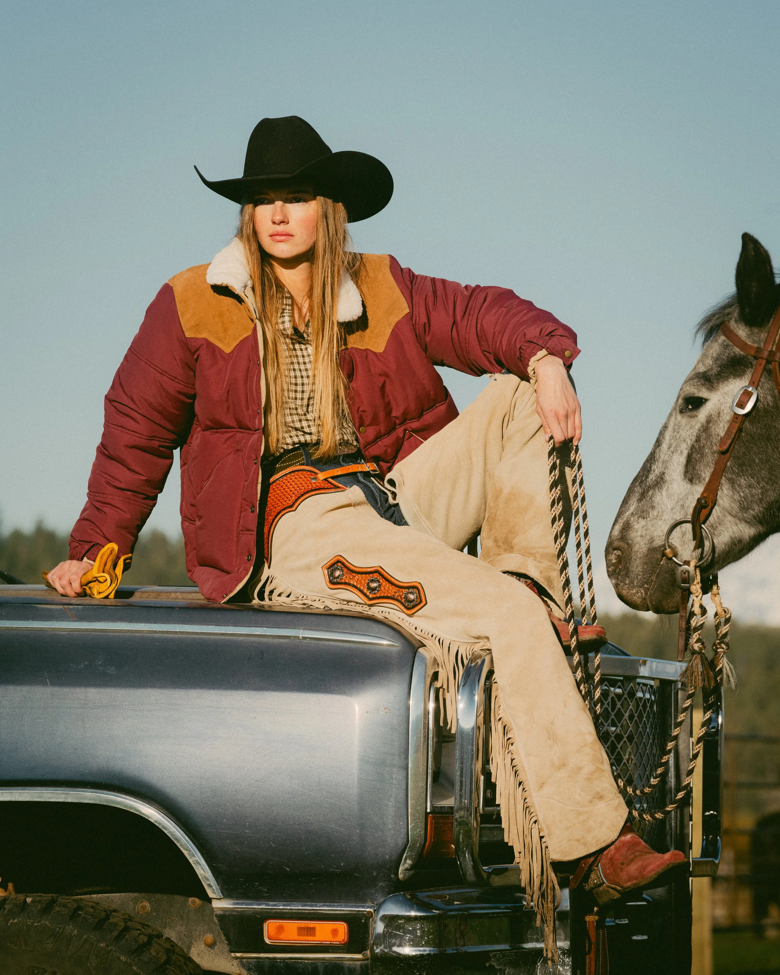 cowgirl sitting on vintage truck hold horse reigns of horse