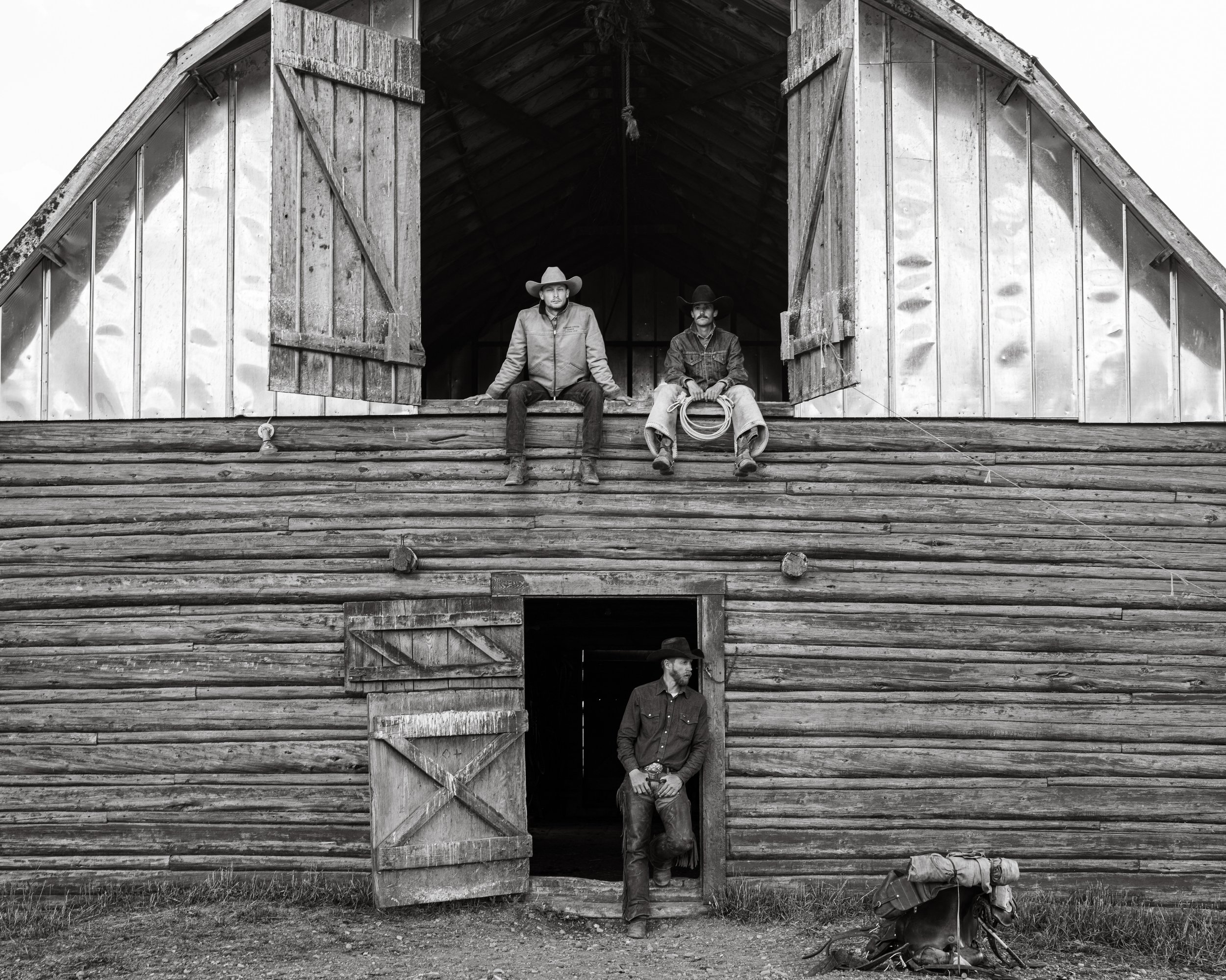black and white photograph of three cowboys and a barn