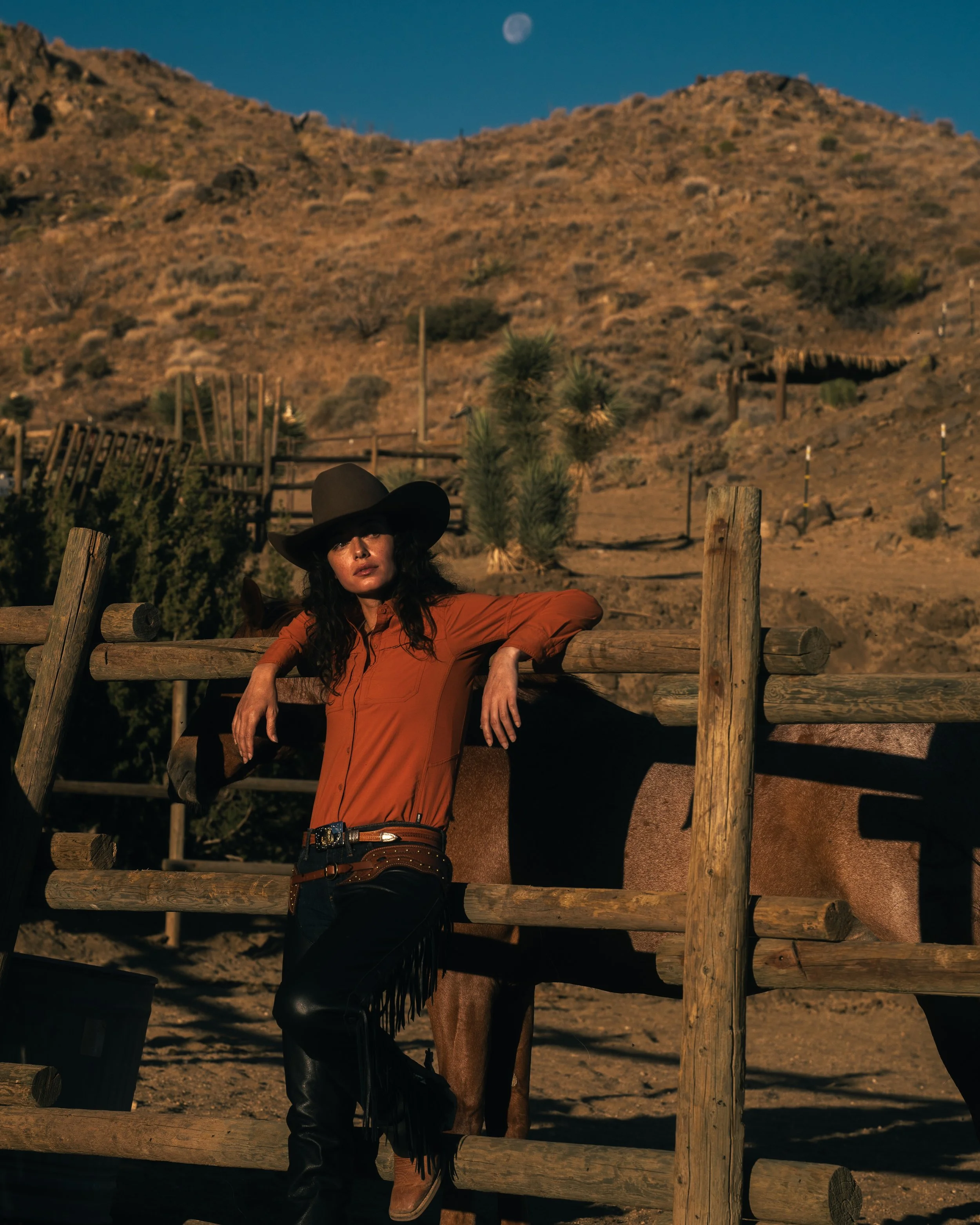 cowgirl posing on ranch fence moon in sky