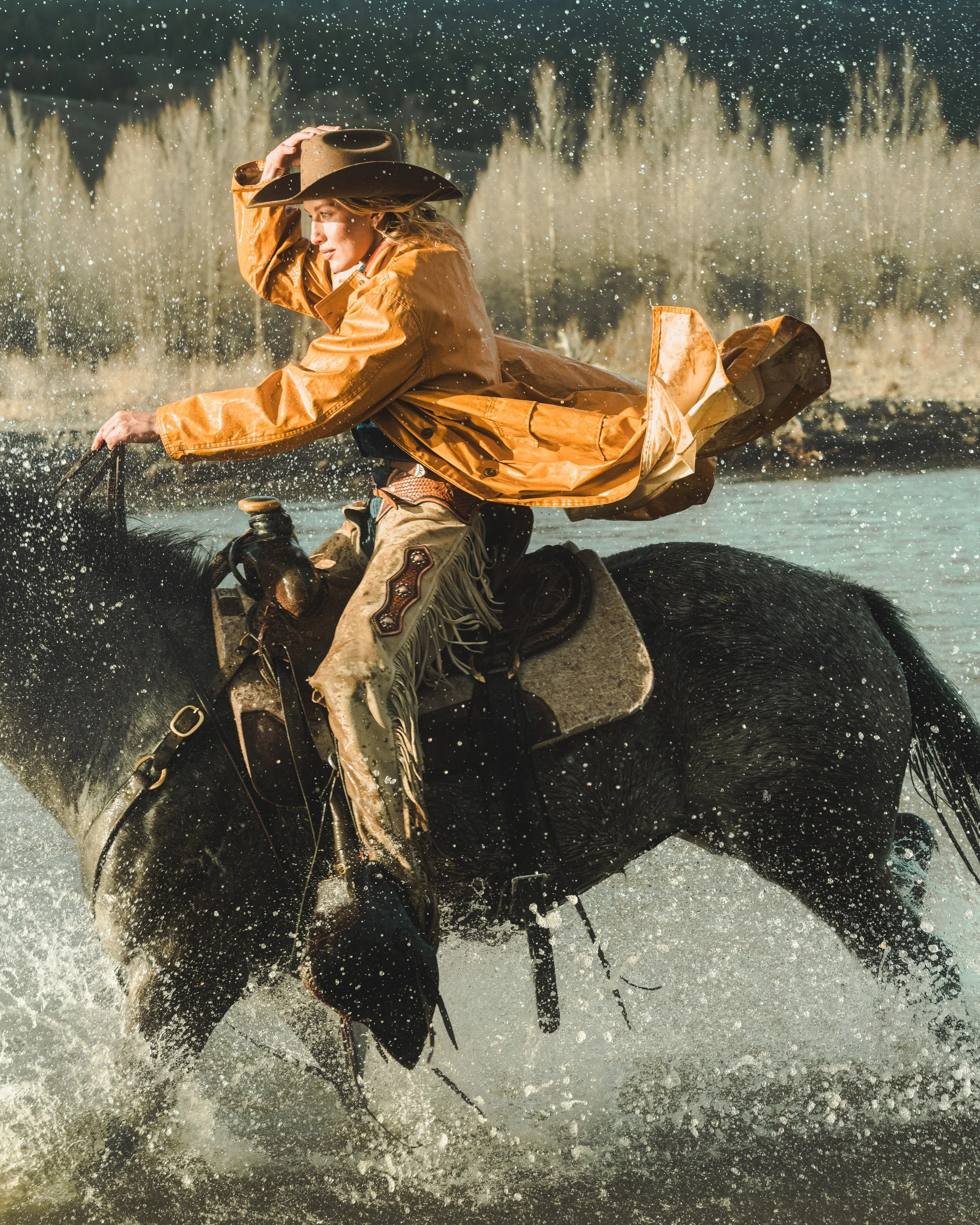 cowgirl riding horse through river with water splashing