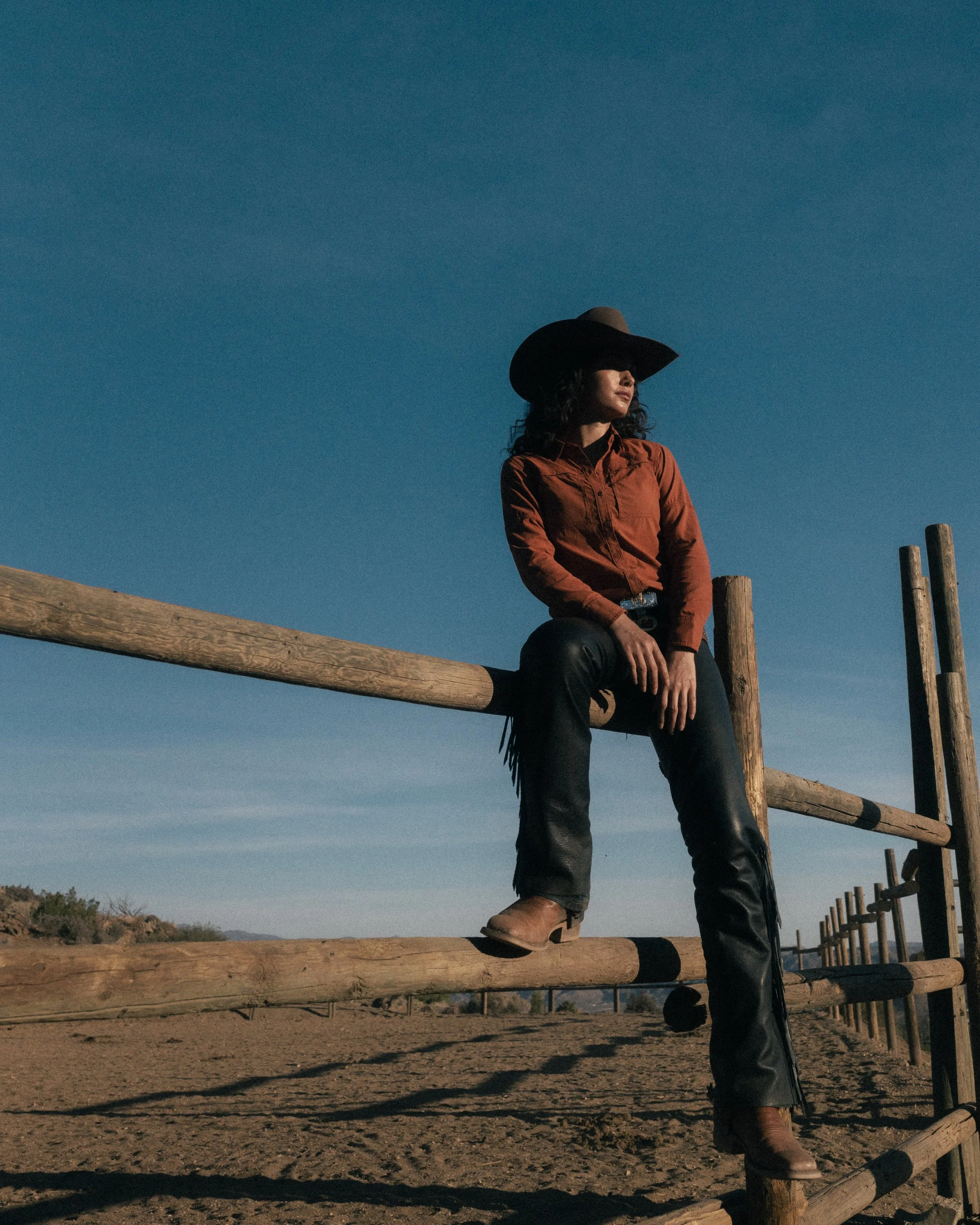 cowgirl sitting on ranch fence