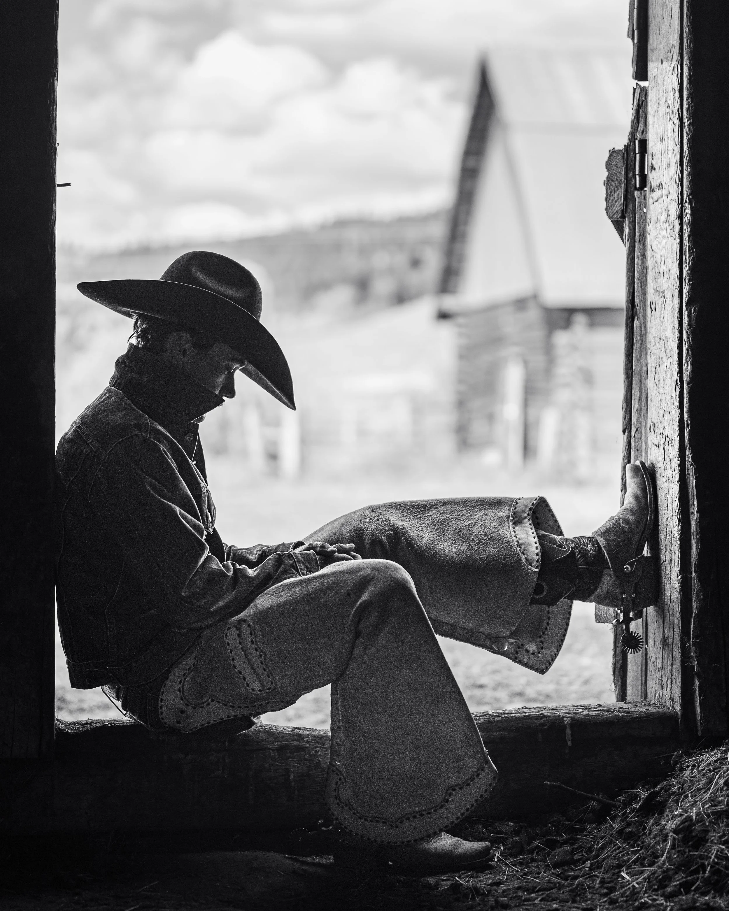 a black and white photograph of a cowboy sitting in a doorway