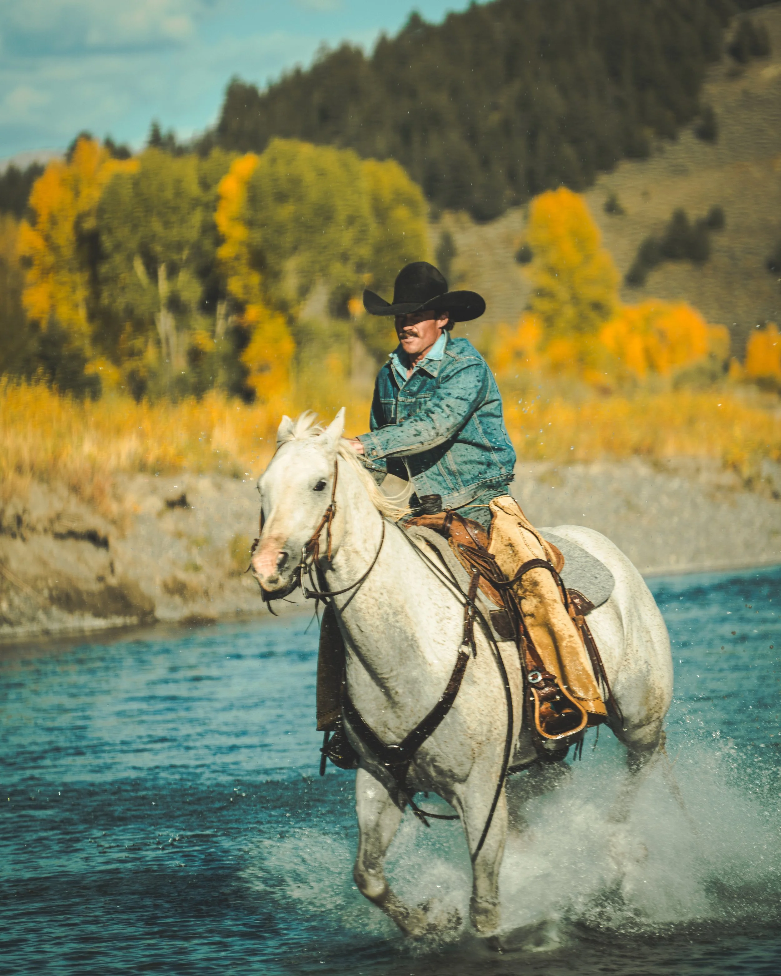 photo of cowboy riding horse through river