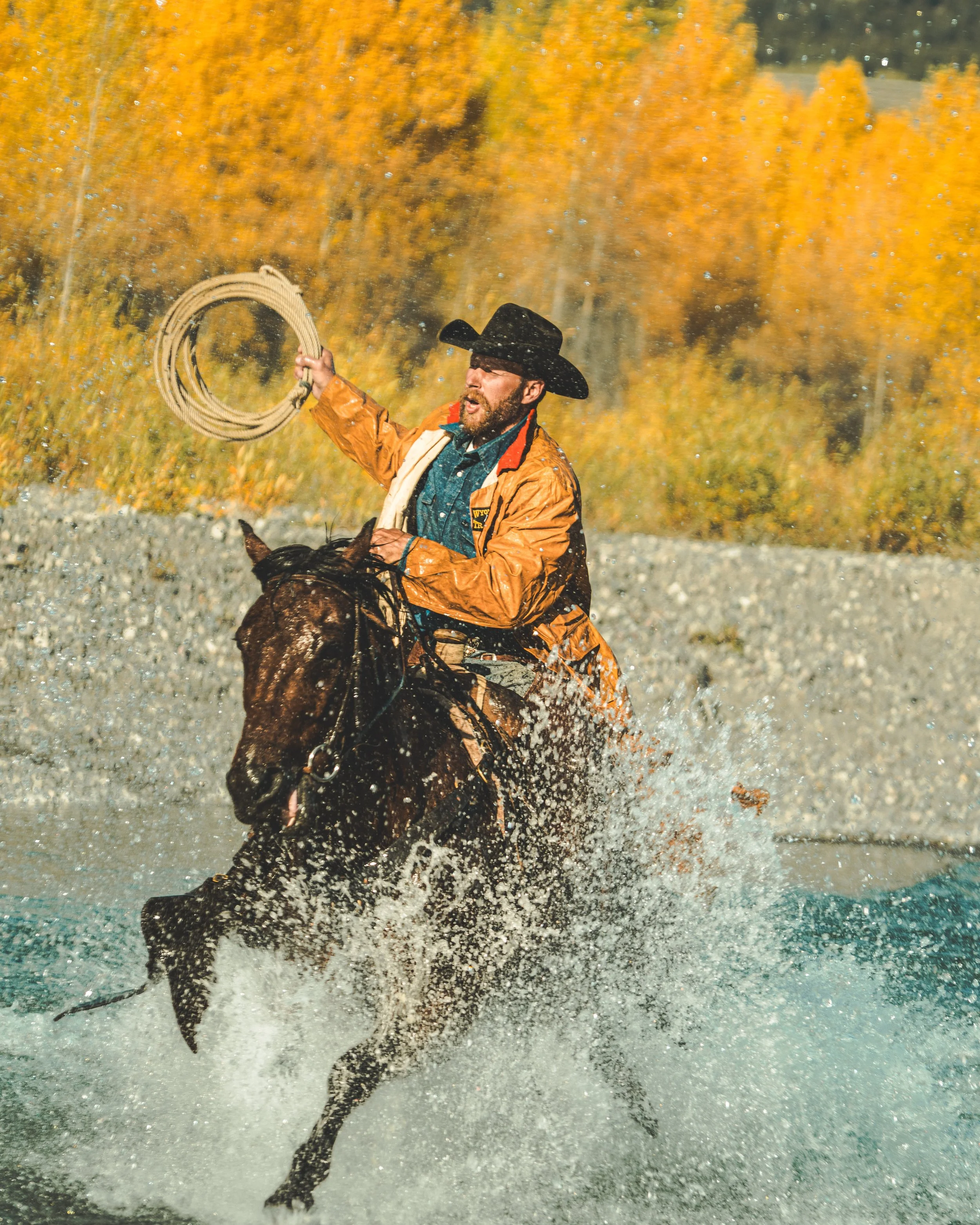 photo of cowboy riding horse through river