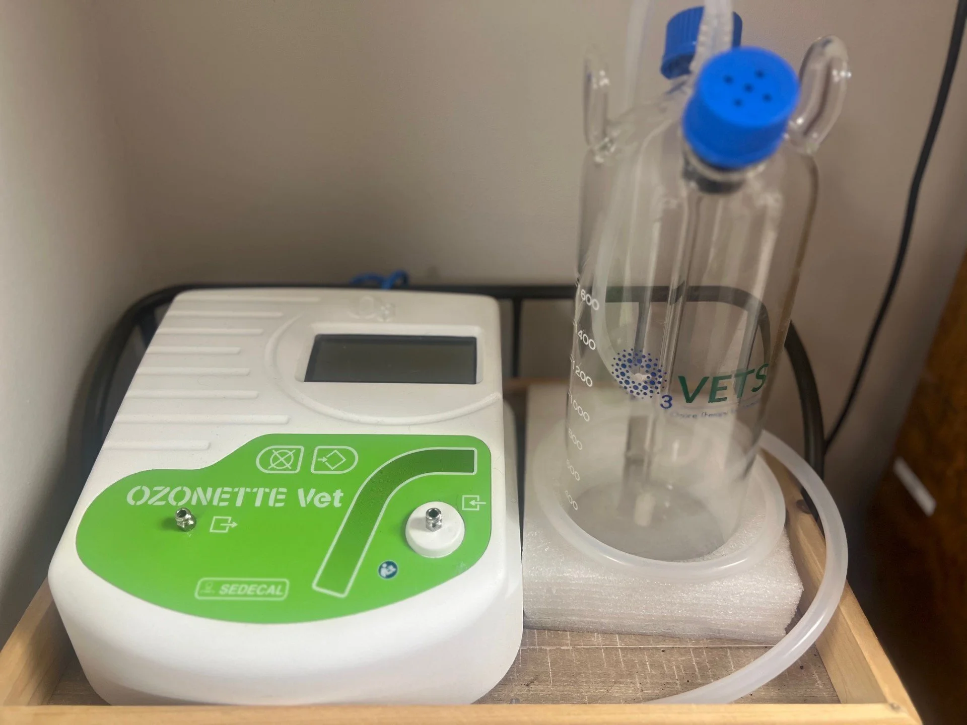 A veterinary ozone therapy machine, a sterile glass water trap with a blue cap, and a plastic tube set up on a wooden tray for pet treatments.