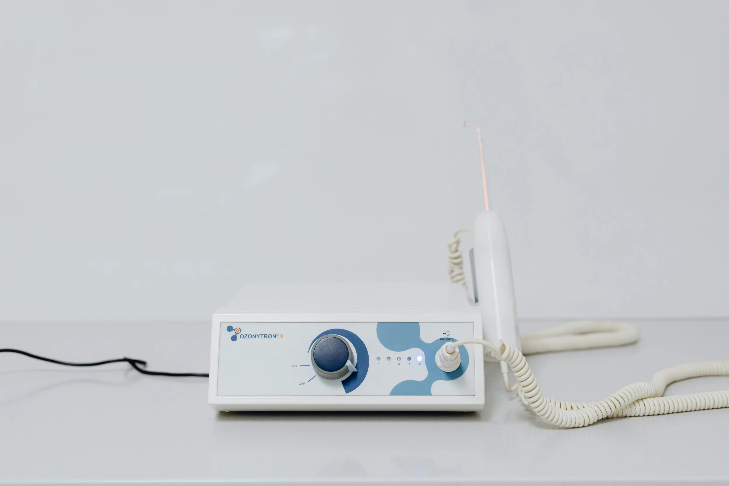 Medical device with a coiled wire and a probe, placed on a white surface.