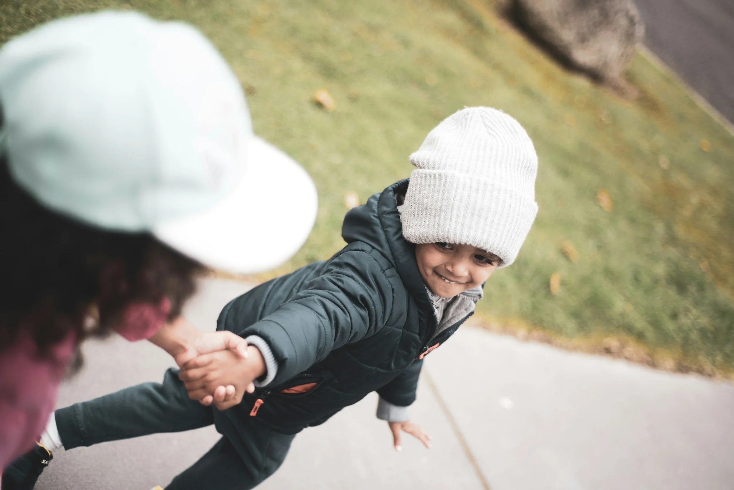 Mother and young child walking together outdoors and holding hands.