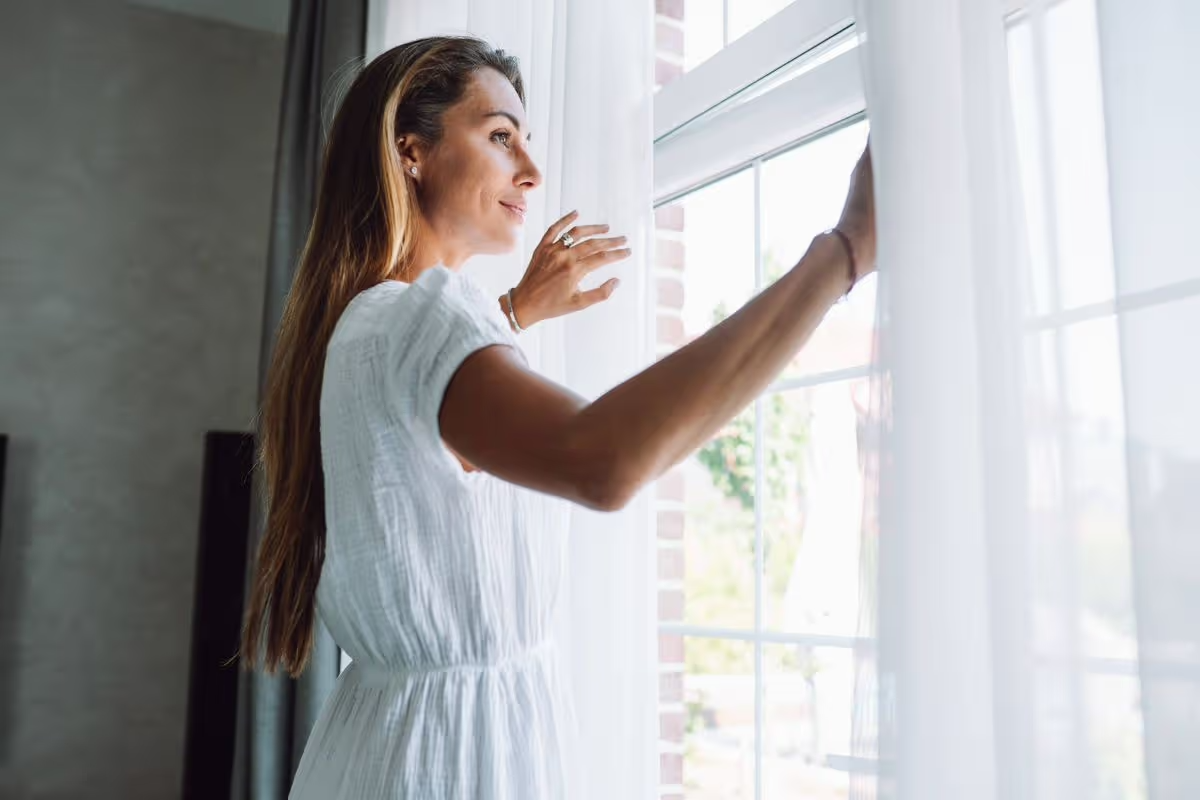 A woman stands in soft natural light with a calm, grounded expression, suggesting relief and openness.