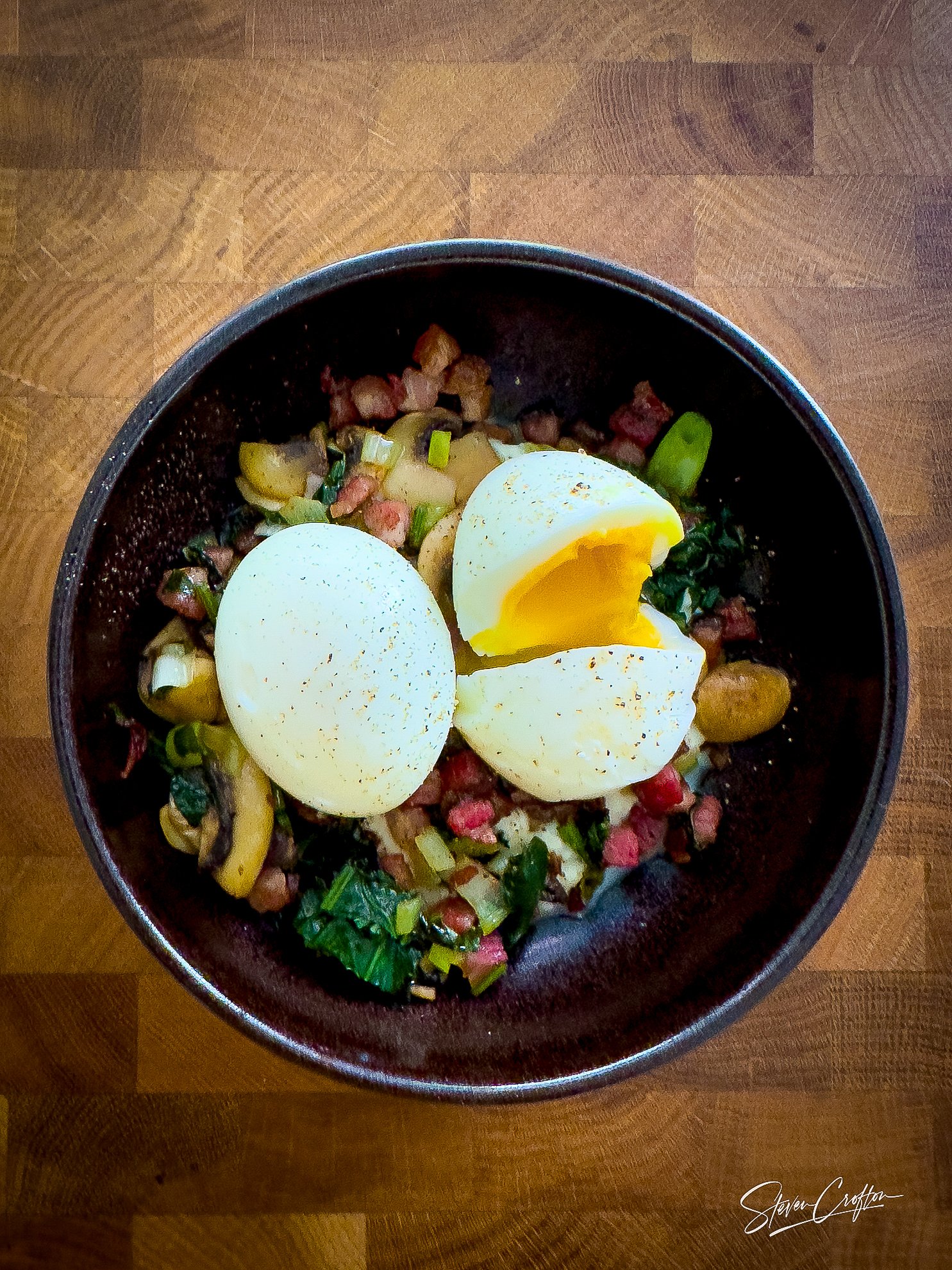A bowl of chopped vegetables, diced bacon, and greens topped with half a boiled egg.