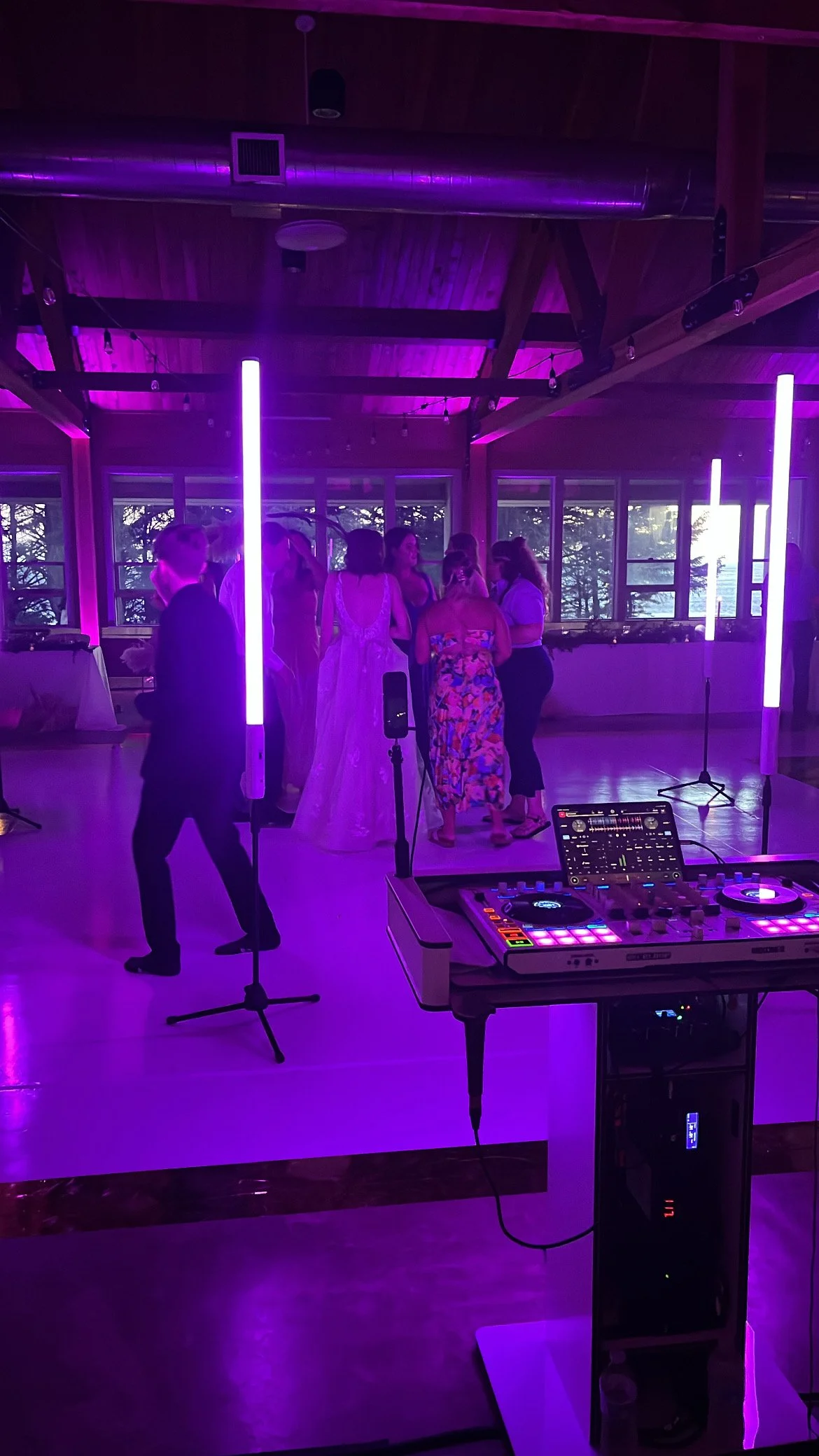 People dancing and socializing in a dimly lit venue with purple LED lights, DJ equipment in the foreground.