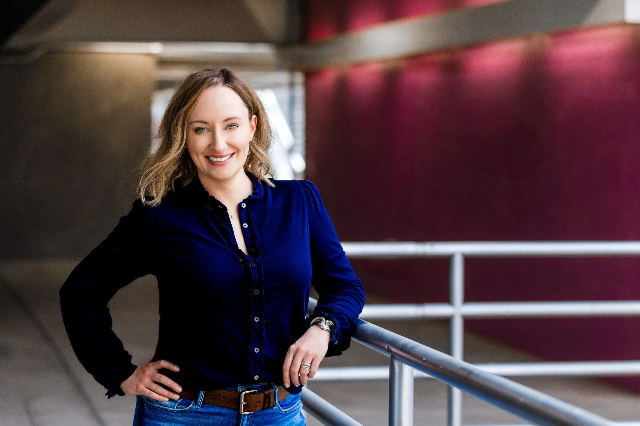 Melissa is looking at the camera, leaning against a metal railing while standing in a parking garage.