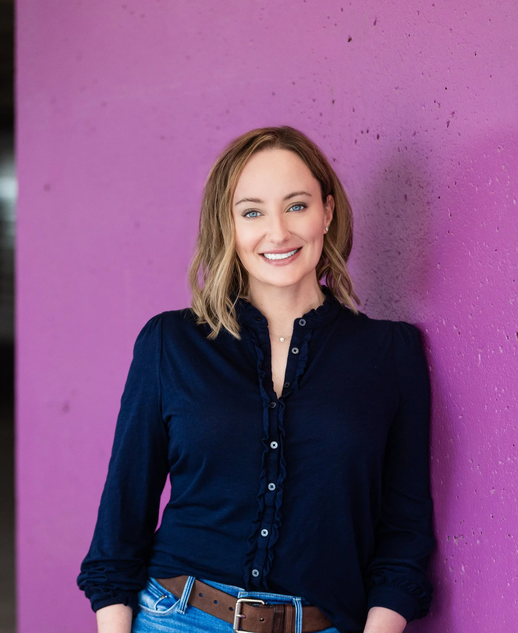 Melissa is standing in front of a purple concrete wall, looking at the camera.